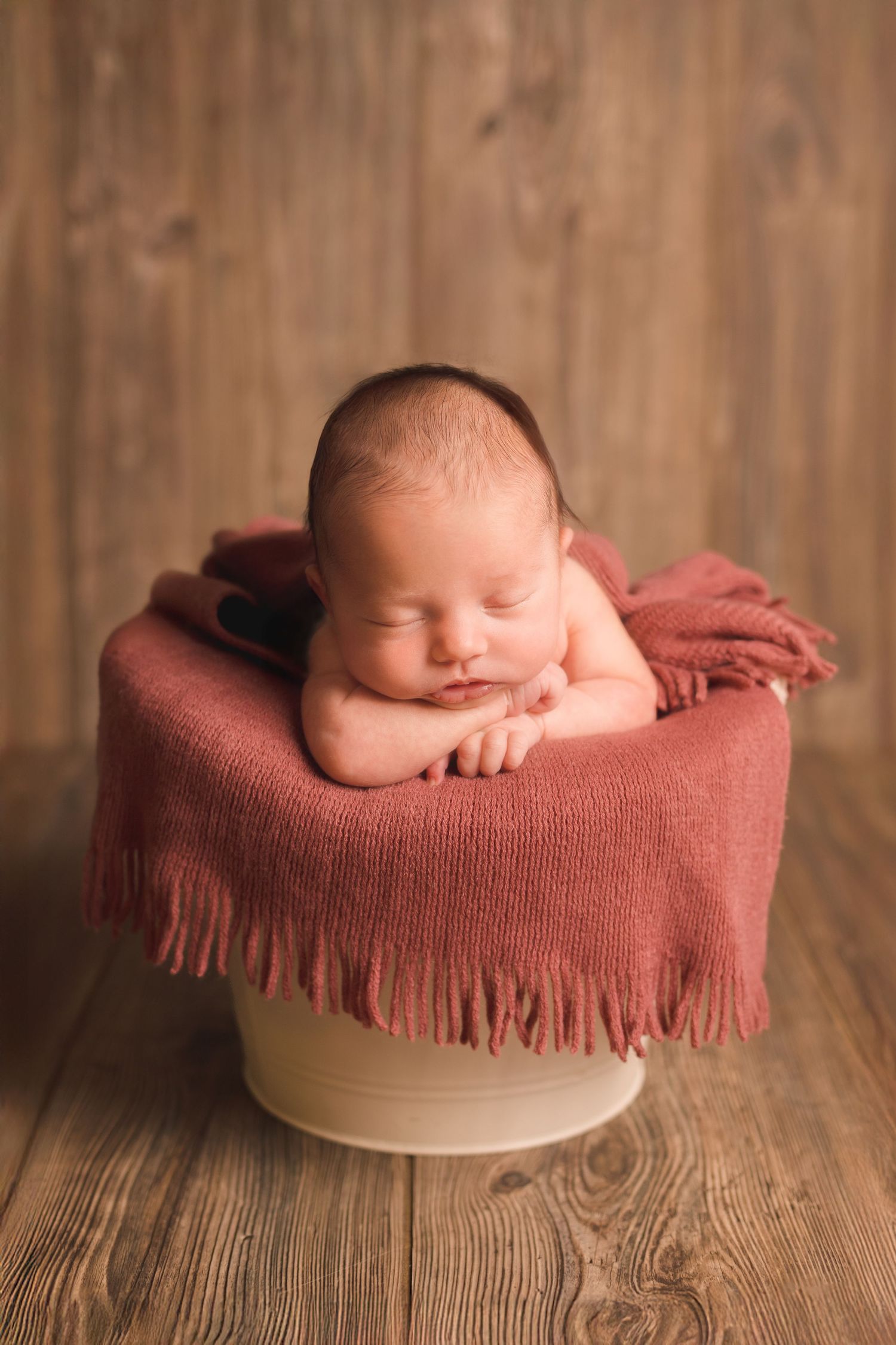 Peaceful newborn sleeping on red textured blanket against wooden background.