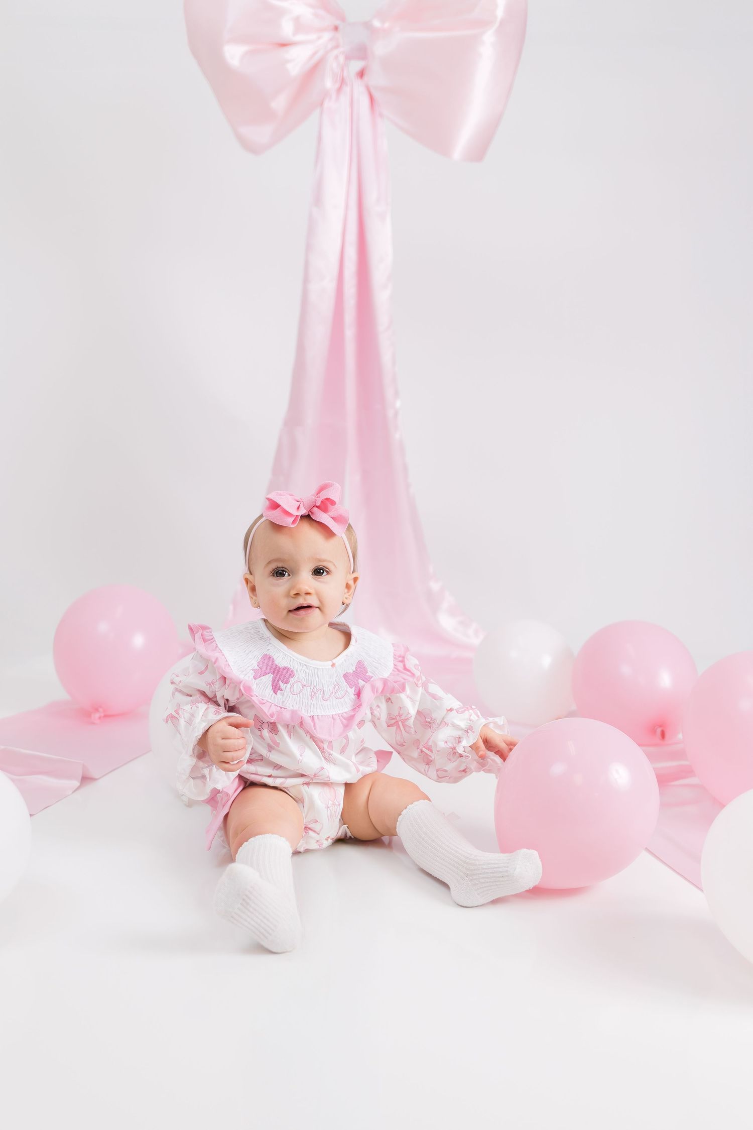 Sweet baby photoshoot setup with pink balloons, bows and decorations against white background.
