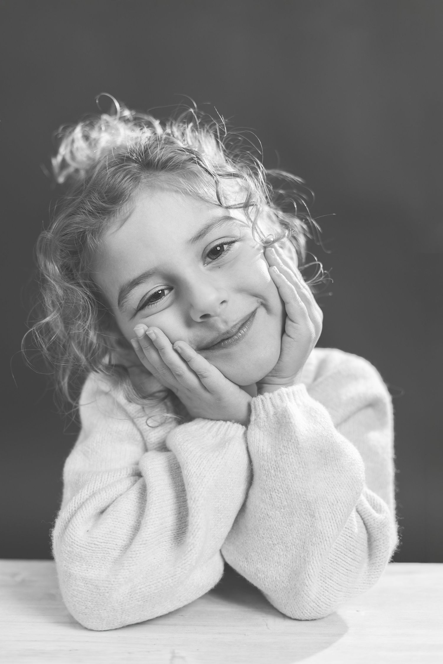A series of black and white portraits showing a child in a white sweater resting their head on their hands with dreamy expressions.