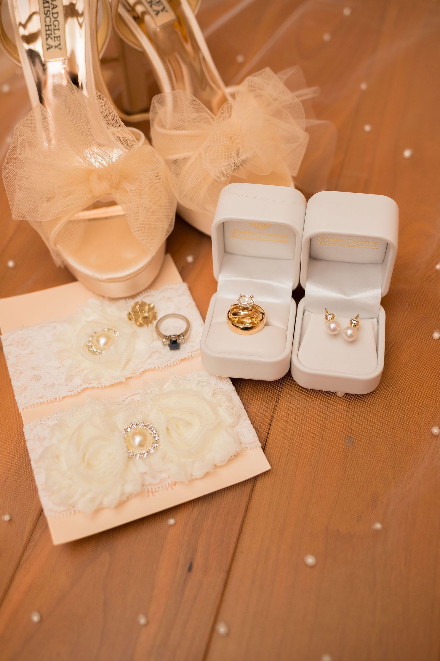 Wedding rings and jewelry displayed on delicate lace against warm wooden background.