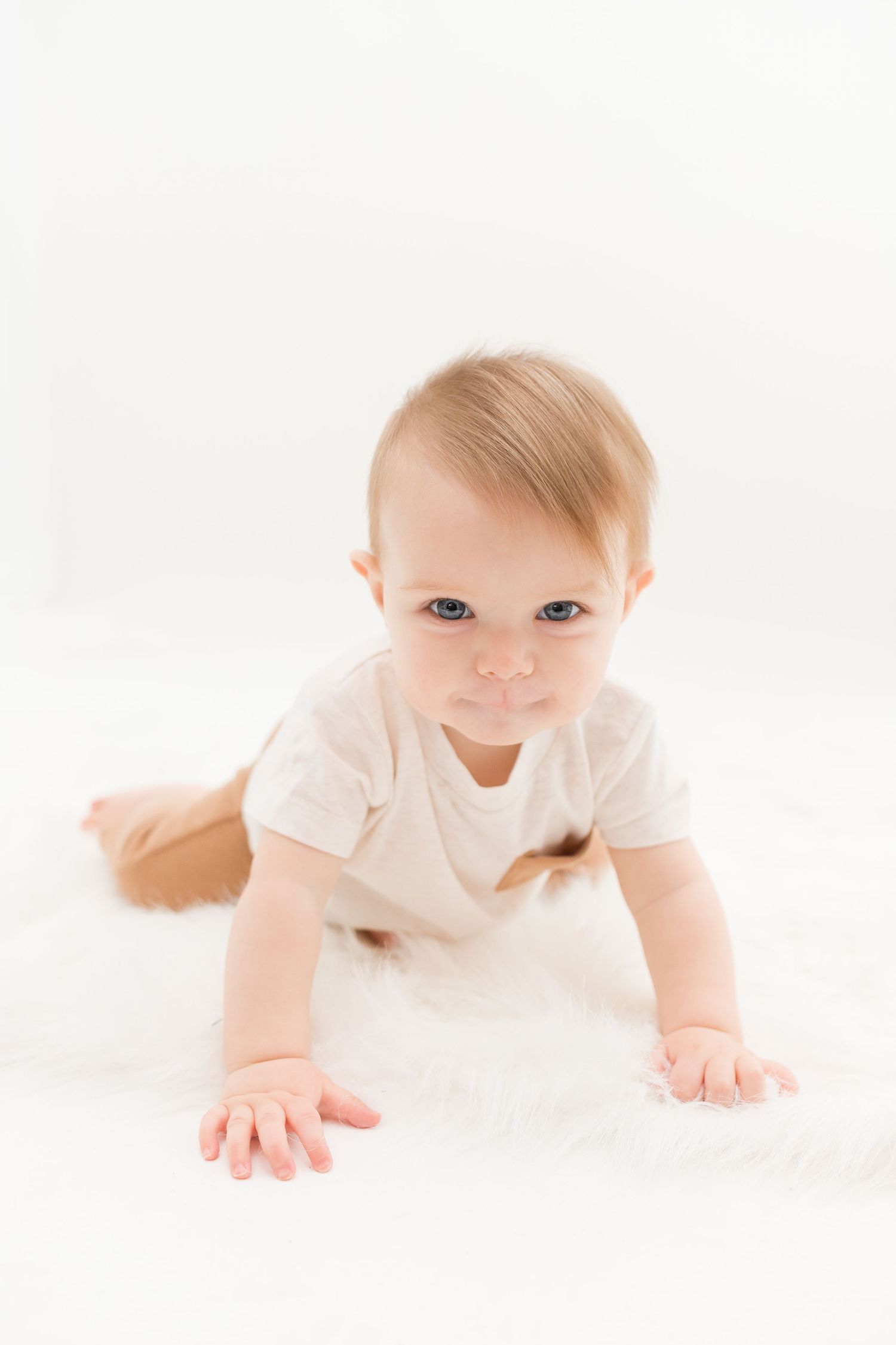 Baby in white outfit crawls on soft white surface in bright studio setting.