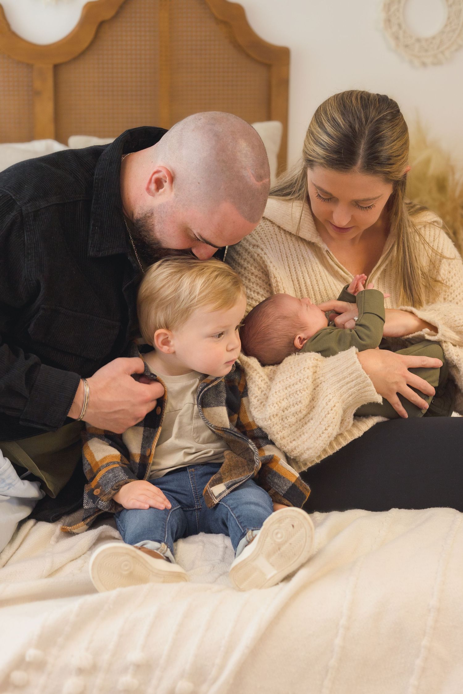 Family lying together on bed sharing intimate moment in cream colored sweaters.