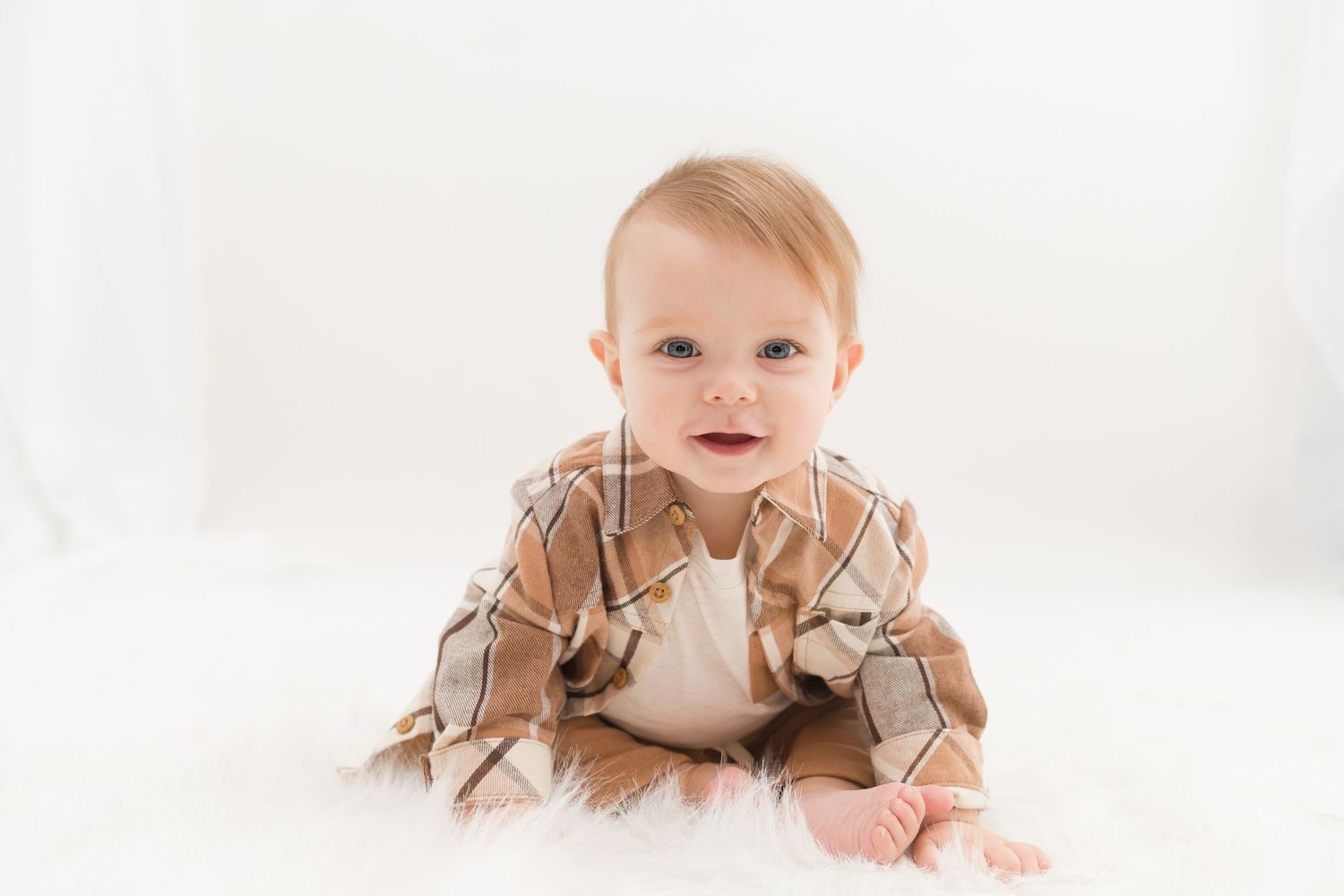 Baby in beige ruffled outfit crawls on white surface.