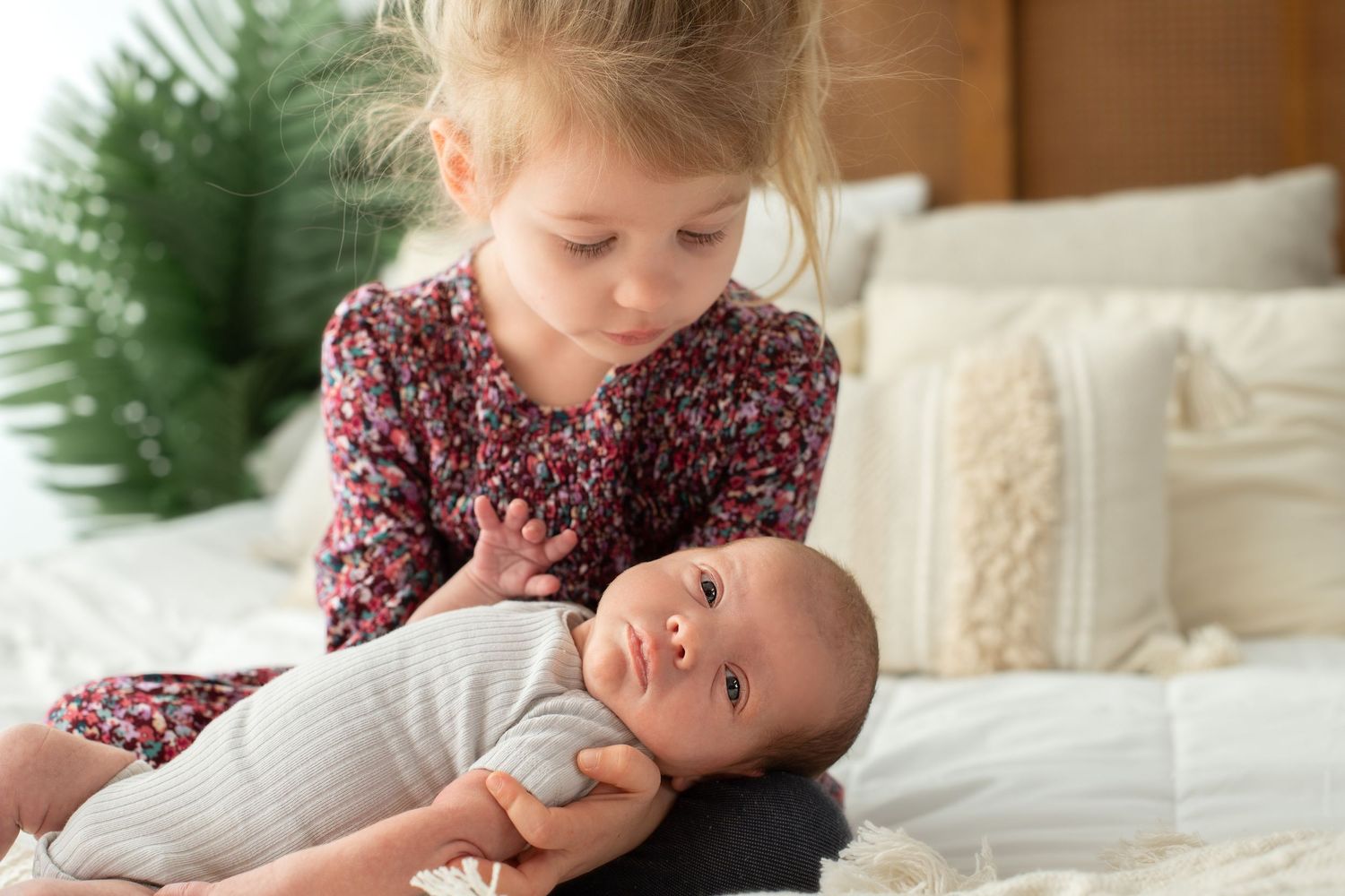 Tender family moment captured on white bedding with greenery in background.