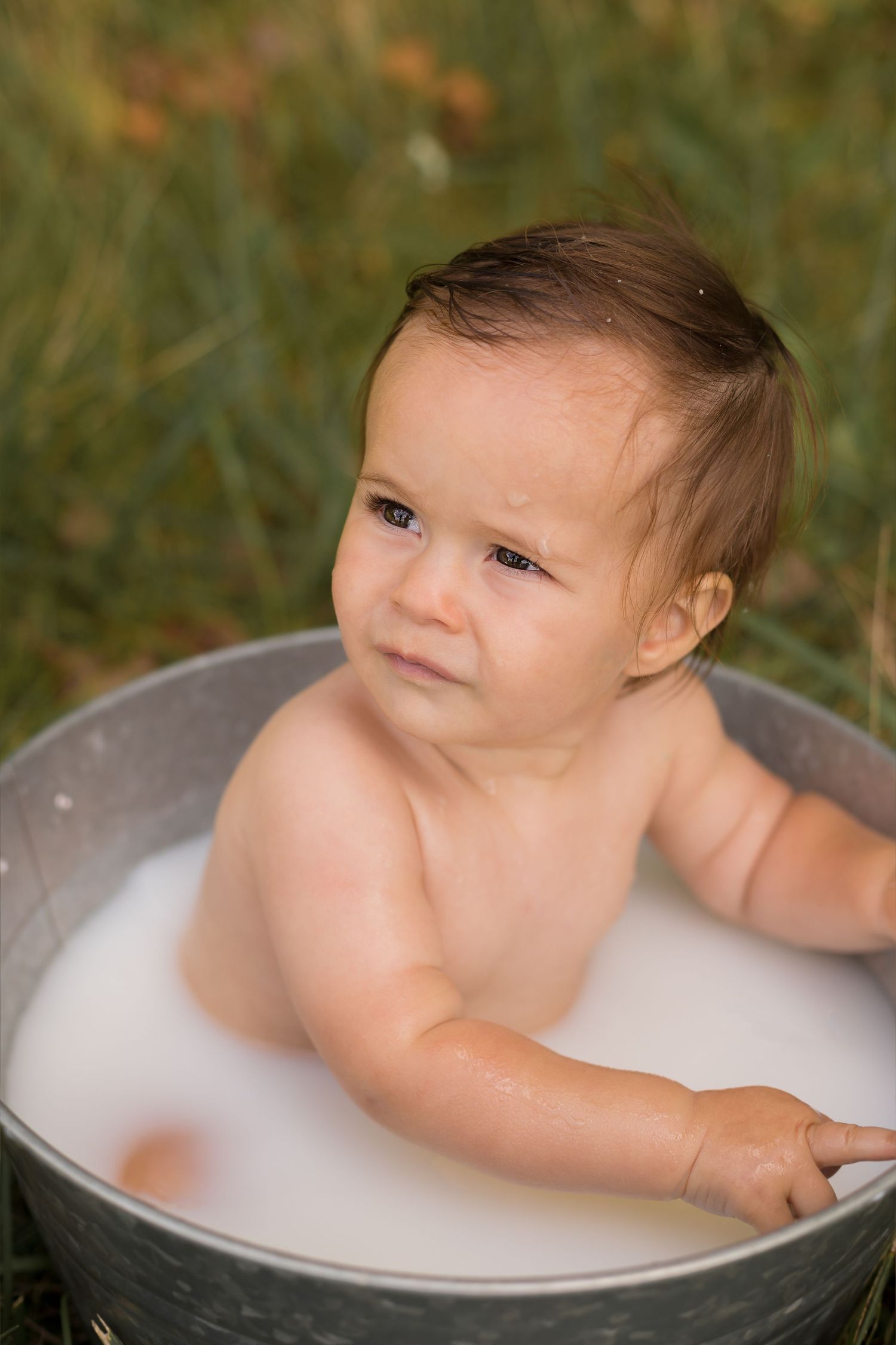 Artistic milk bath portrait in a vintage metal tub surrounded by natural grass.