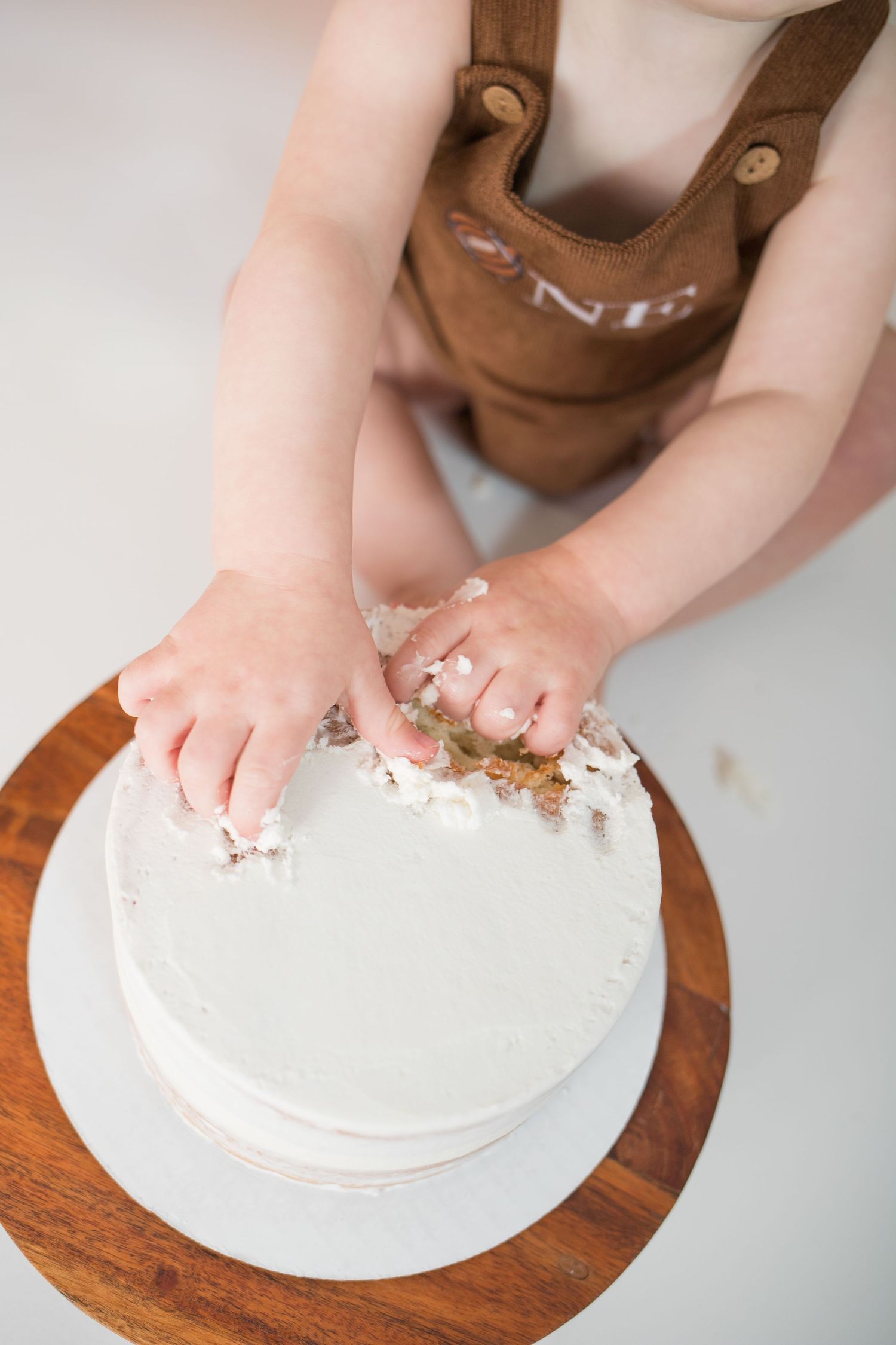 Small hands reaching to touch white frosted cake on wooden board.