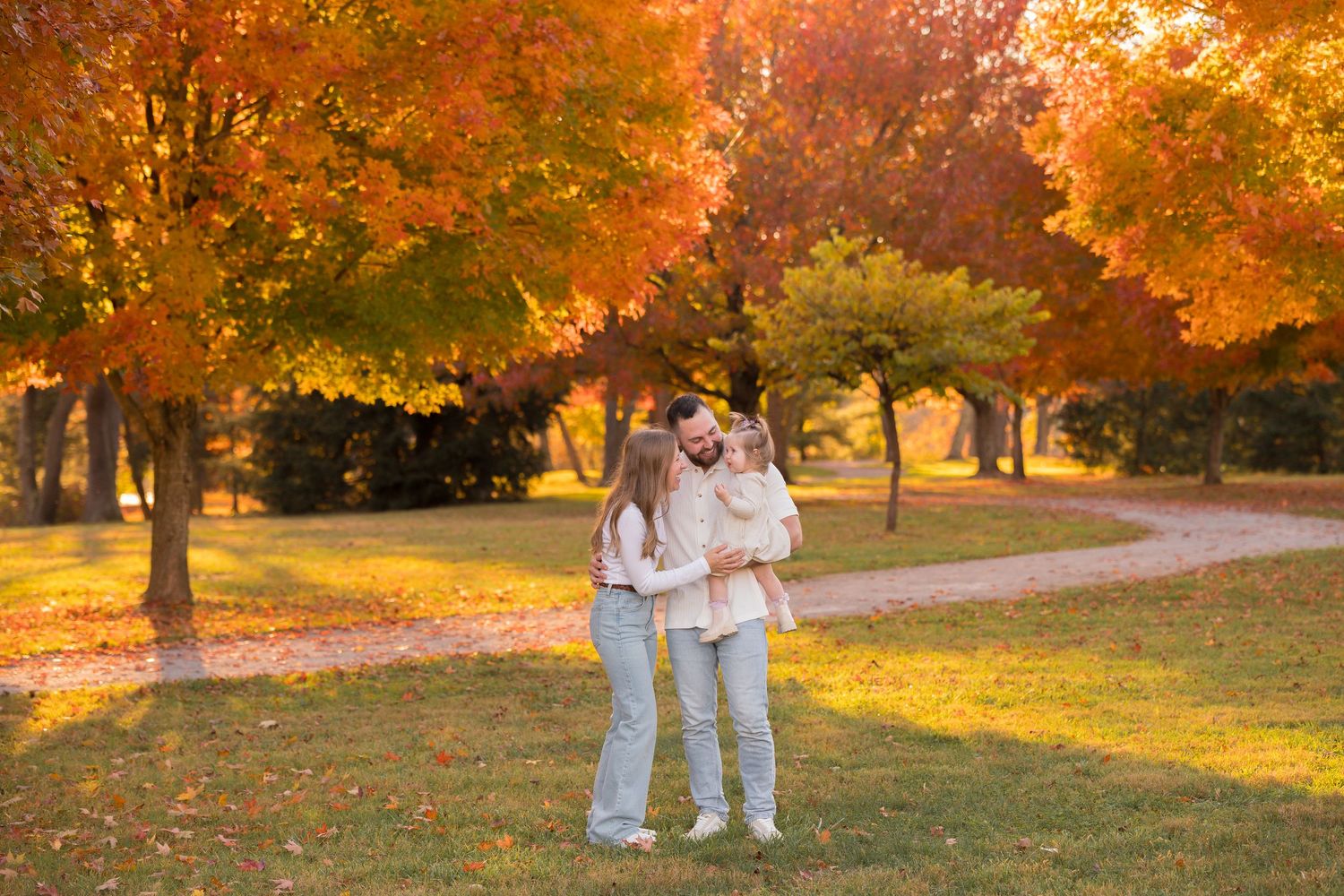 People gather under bright orange fall trees during sunset in a park.