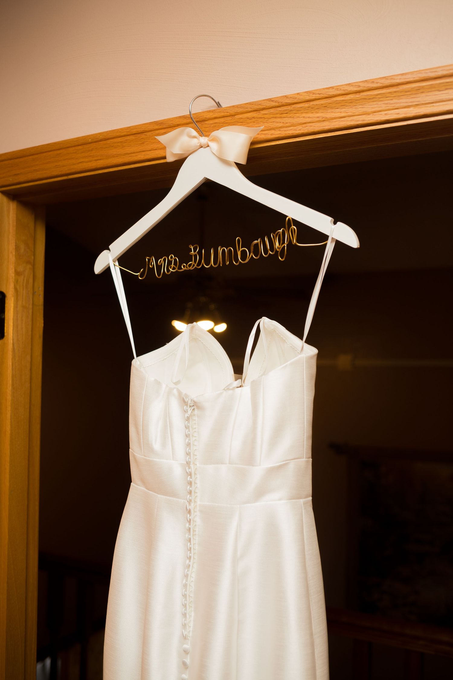 White wedding dress hanging on personalized hangers against dark wooden backdrop.