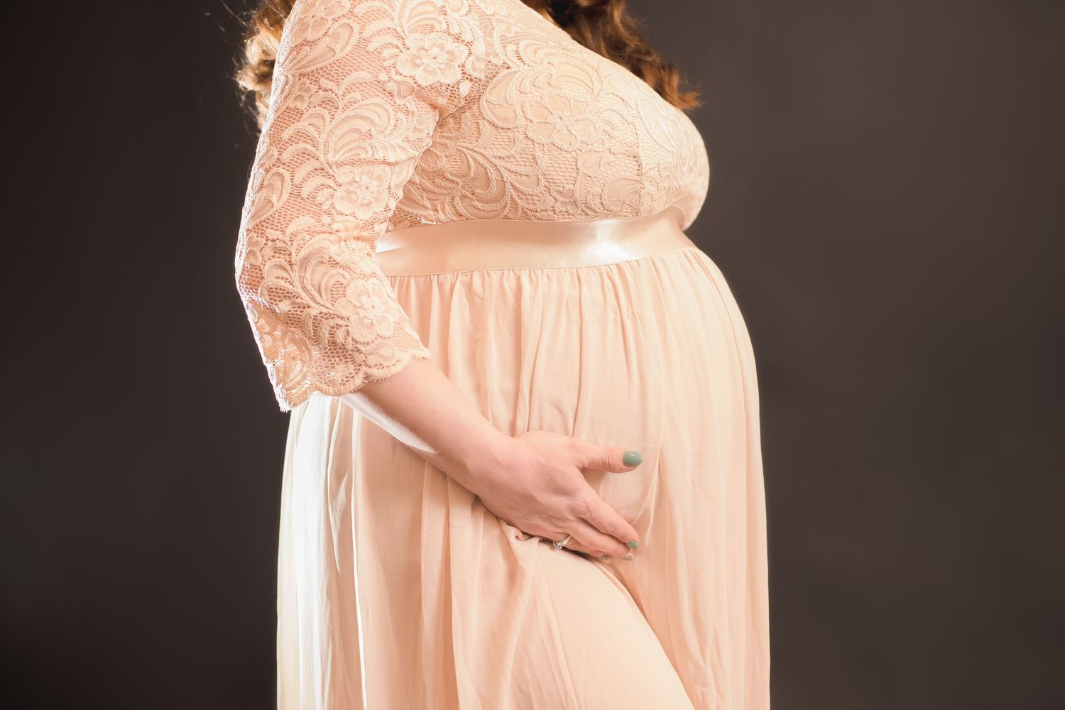 Elegant peach maternity gown with lace details photographed in studio setting.