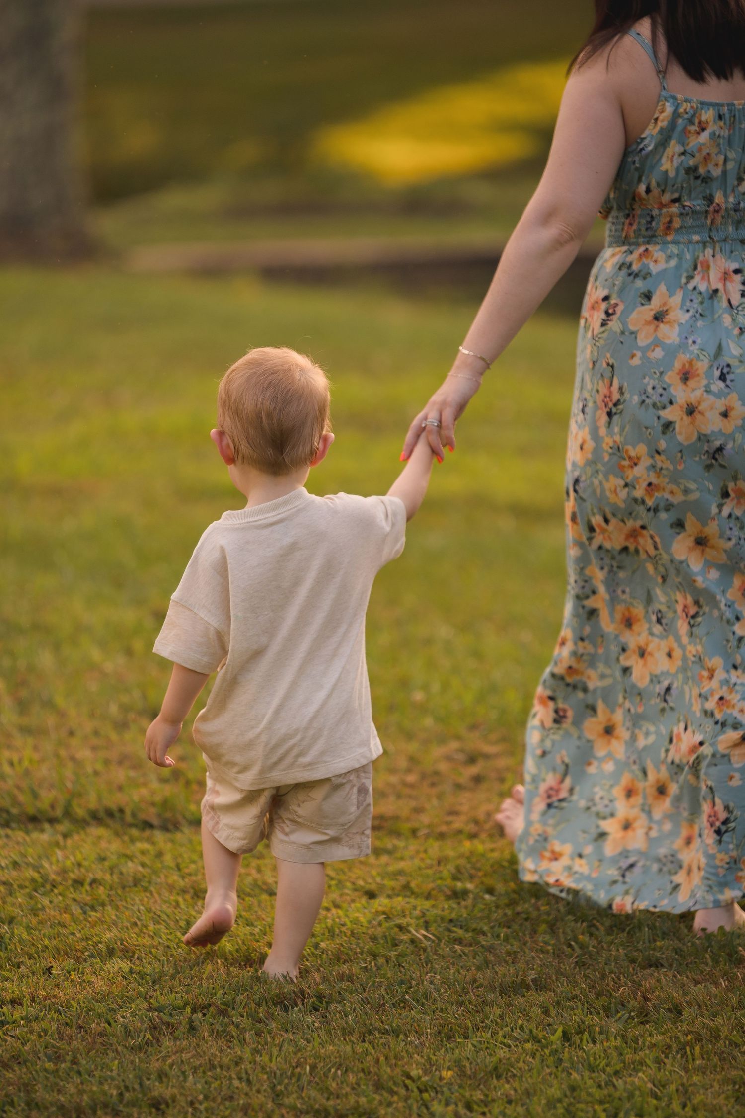 A toddler walks through green grass wearing light colored clothing.