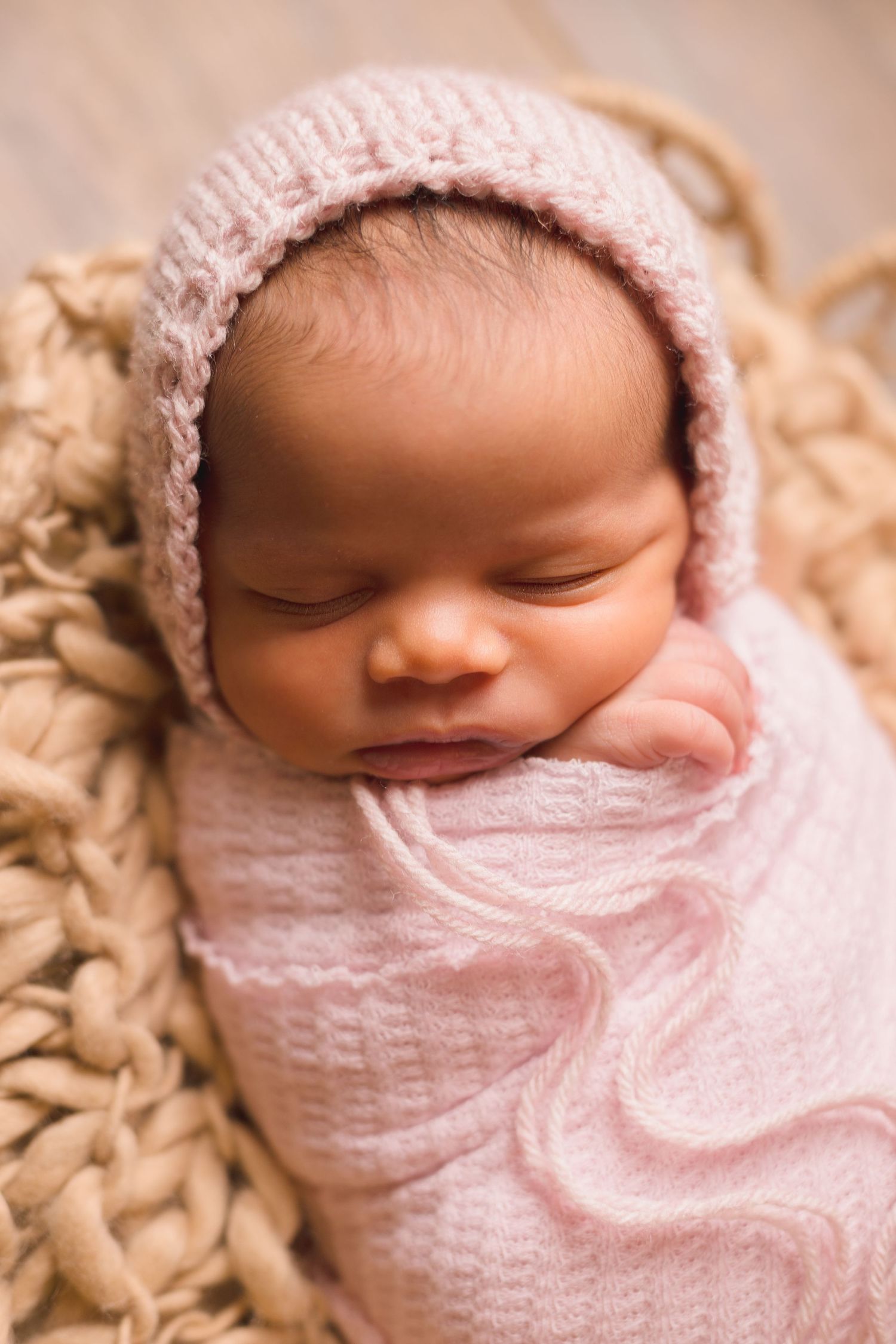 Delicate newborn photography with pink lace bonnet and soft white wrap.