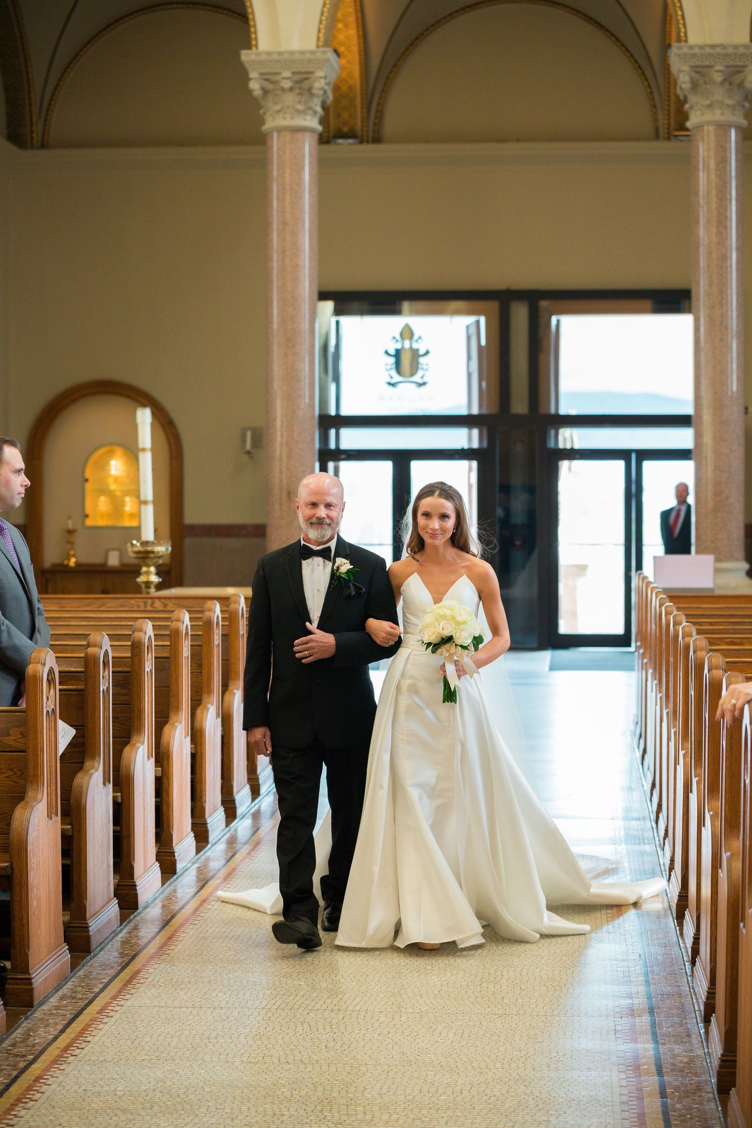 Wedding ceremony in progress down center aisle of traditional Catholic church.