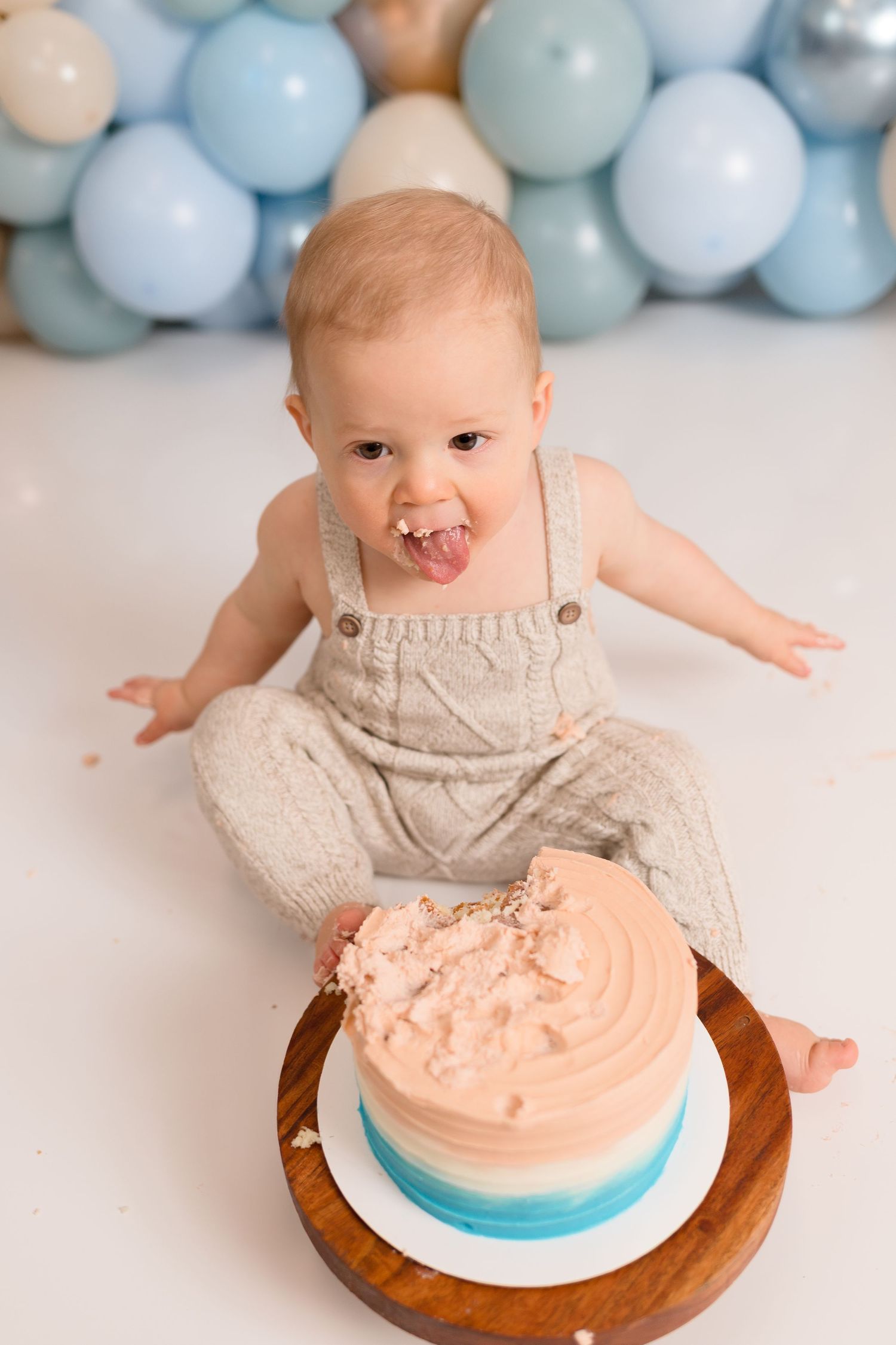 Baby in knit romper reaching for peach and blue birthday cake.