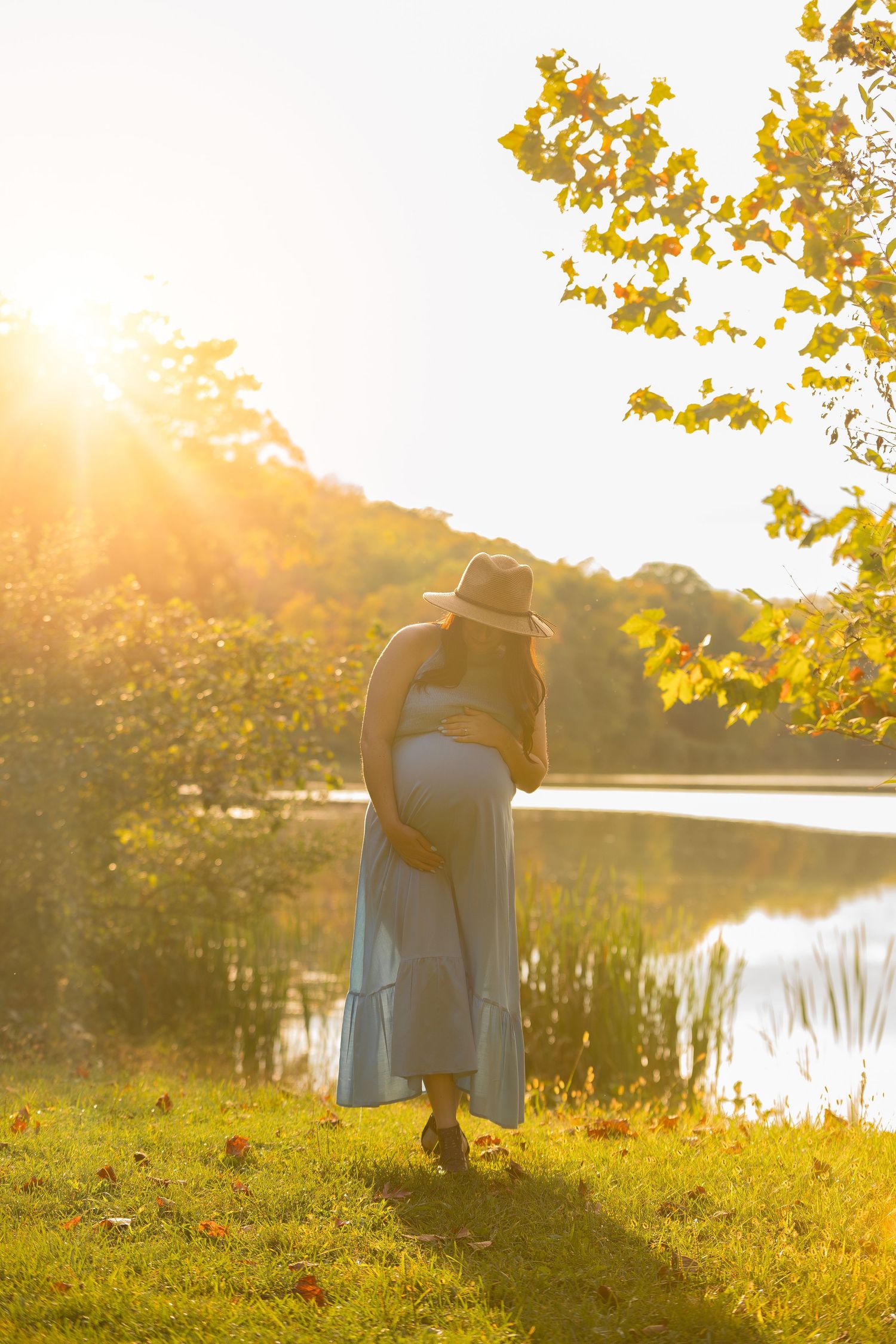 Couple in autumn setting by lake during golden hour with sun flare and fall foliage.