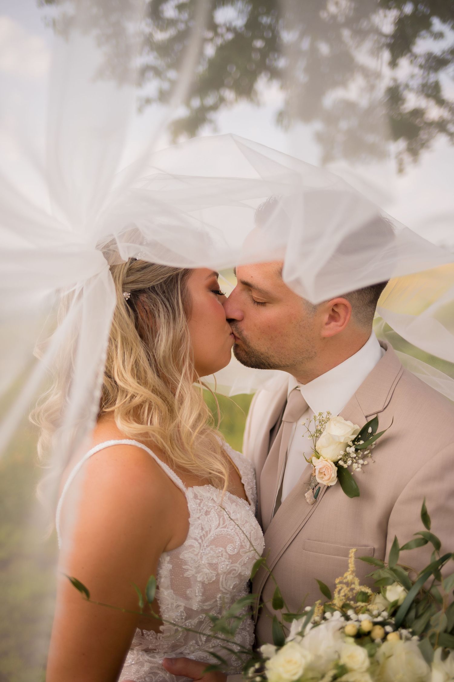 Romantic wedding portrait under a flowing veil in natural outdoor setting.