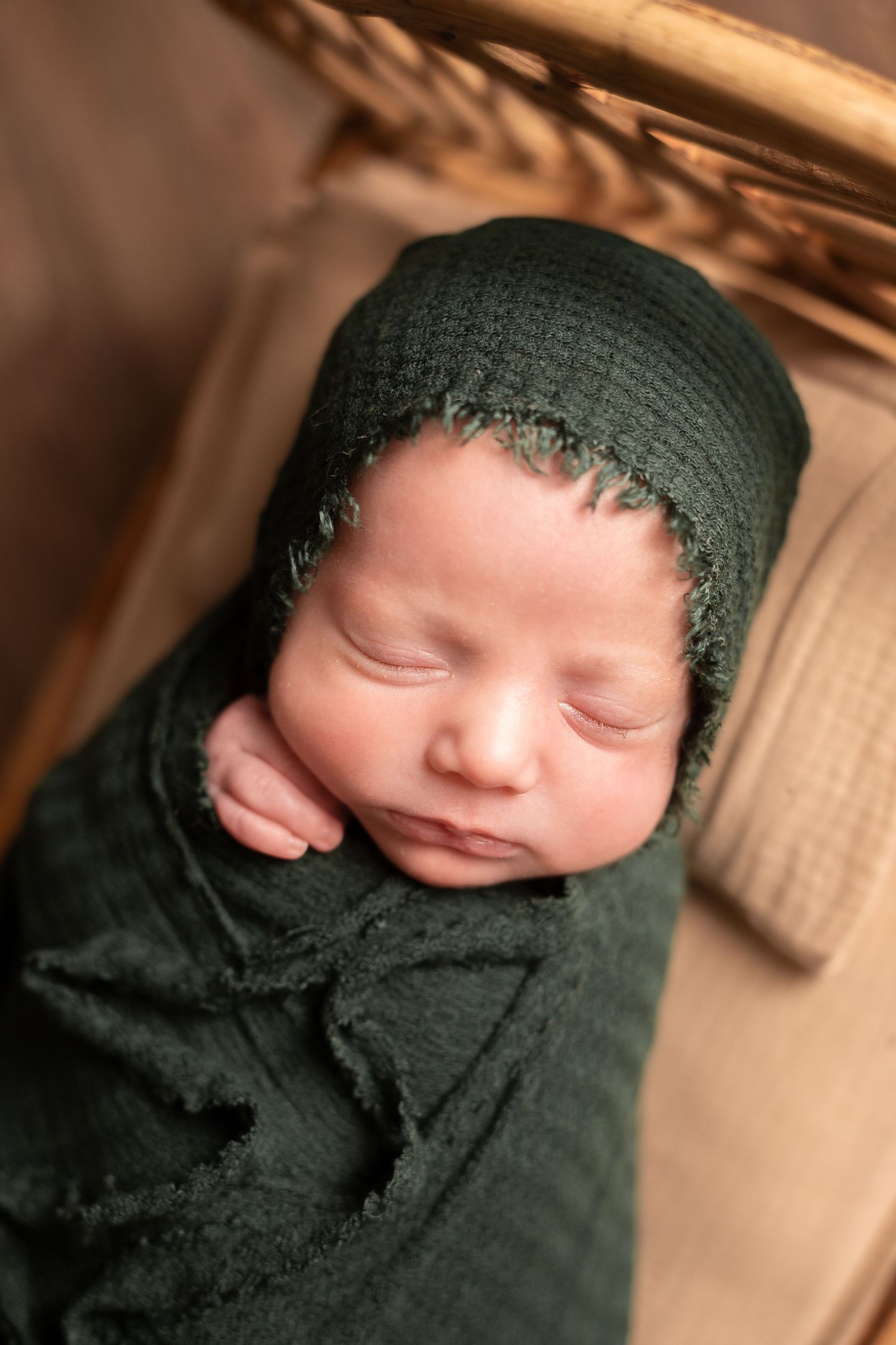 Sleeping newborn wrapped in dark green fabric shown in artistic portrait series.