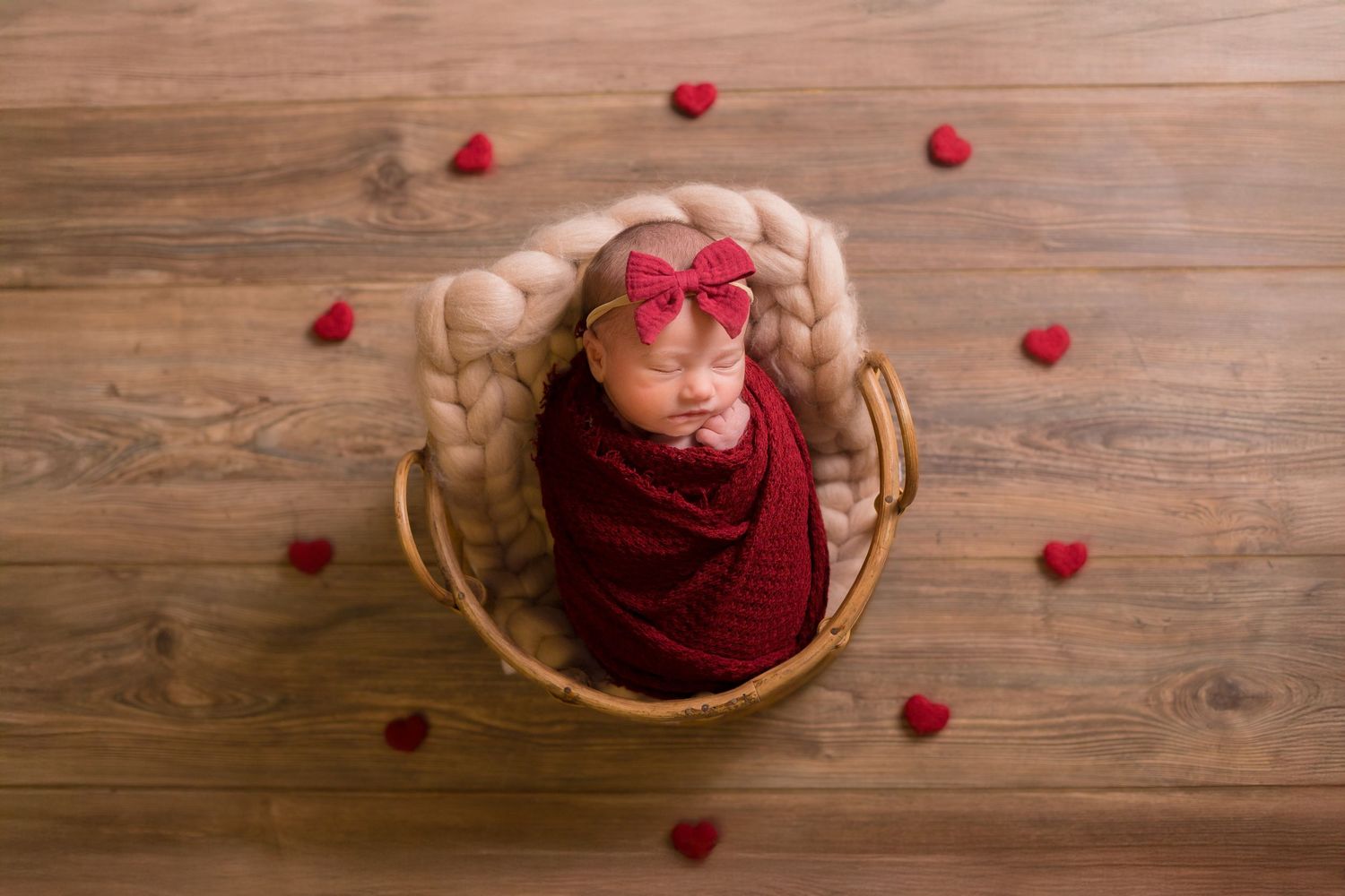 Newborn photography setup with red hearts scattered on wooden floor.