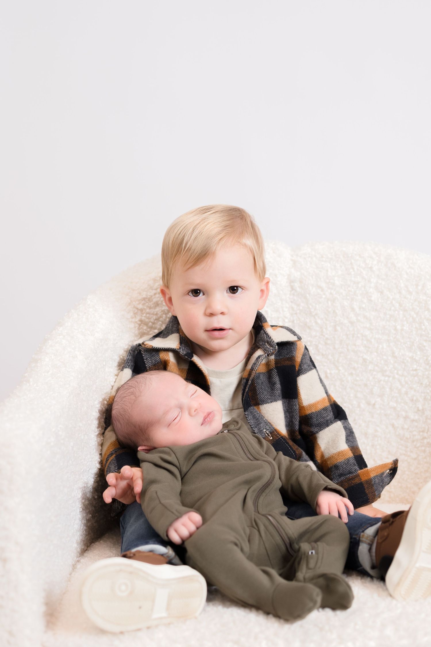 Two children on white backdrop, one in plaid shirt and one in olive green outfit.