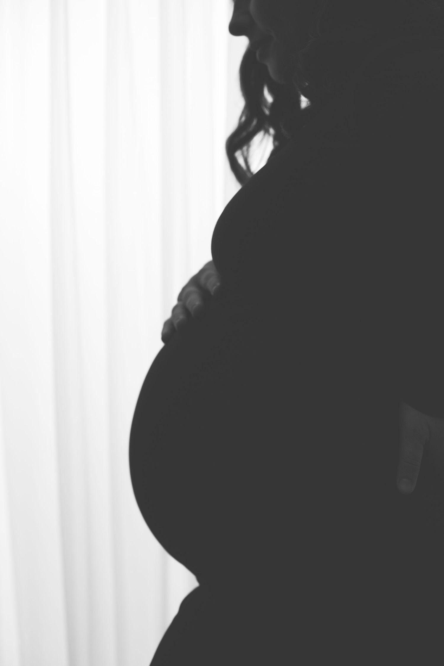Artistic silhouette maternity photos showing pregnant belly against white curtain background.