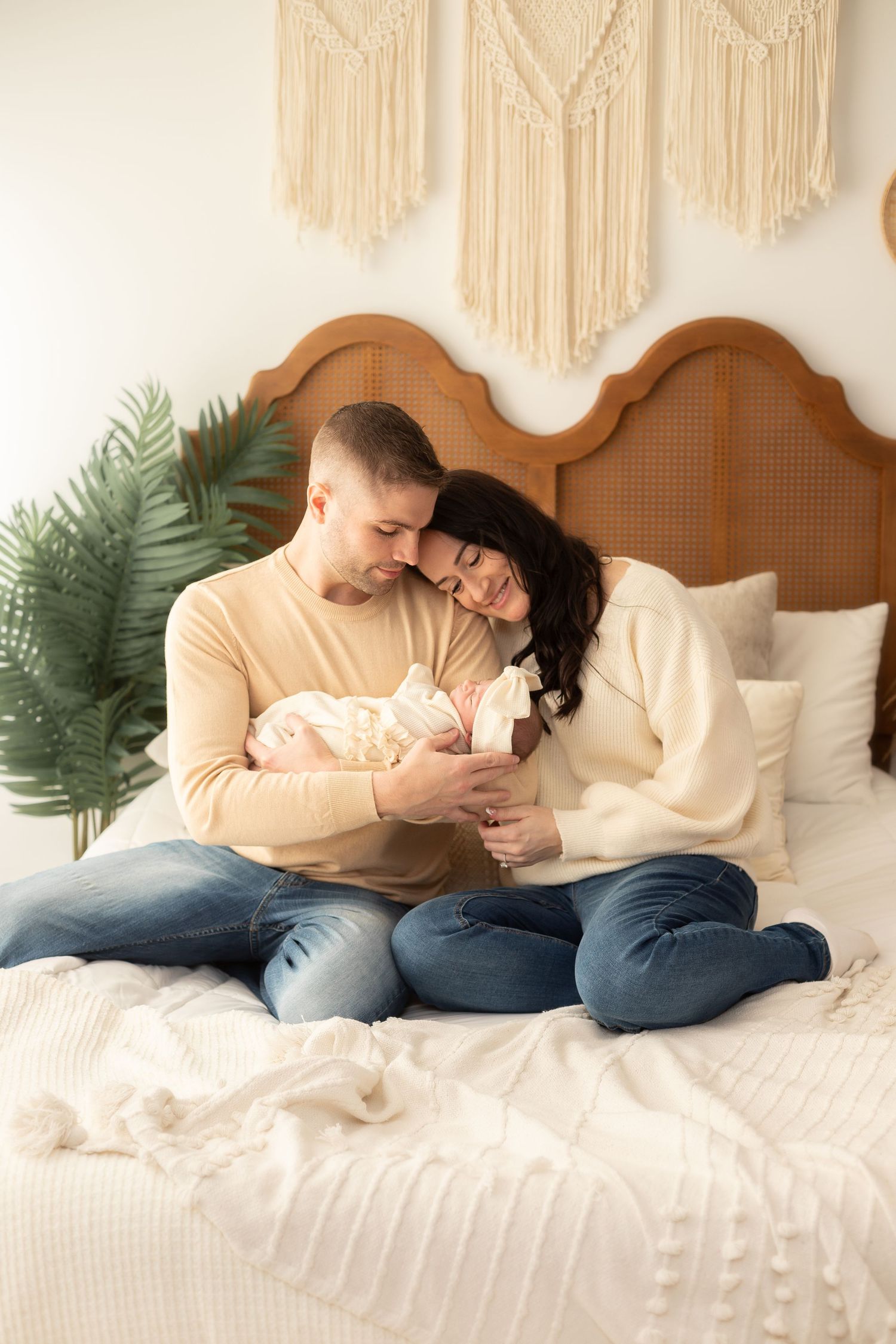 Couple sharing intimate moment together on white bed with macrame wall decor and plants.