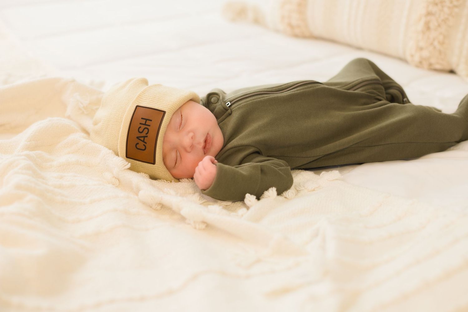 Infant resting on white bedding wearing olive green outfit.