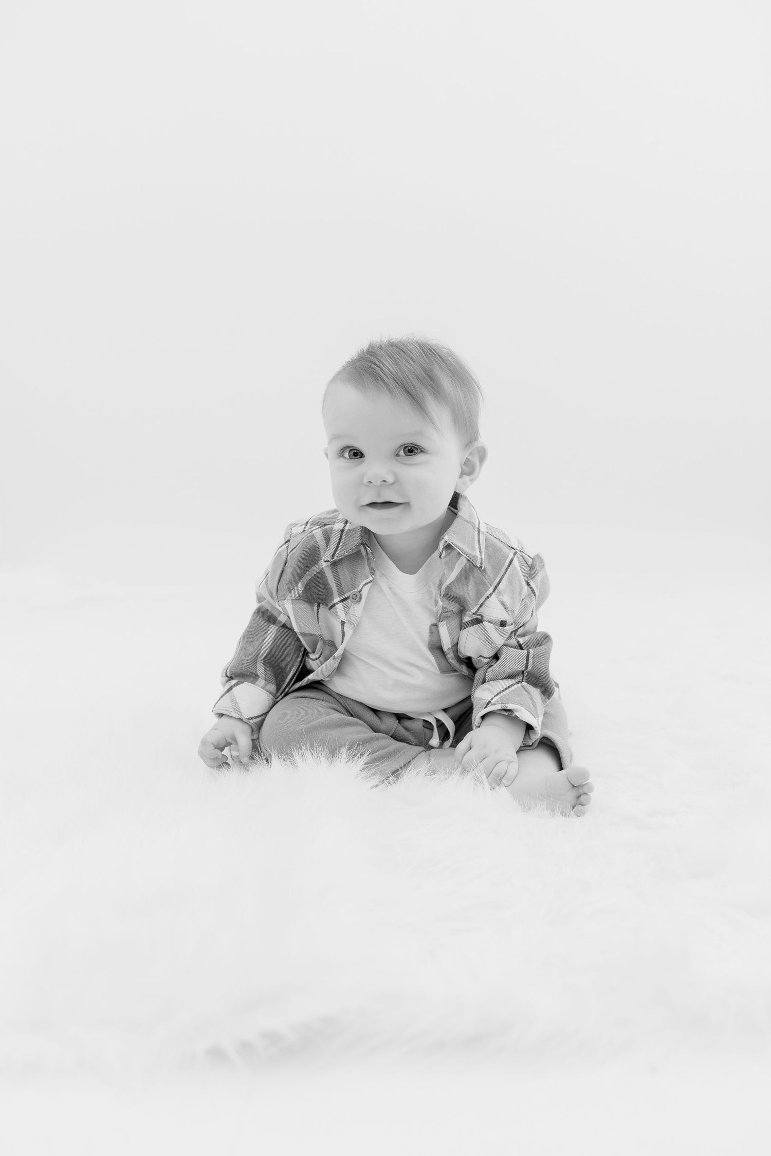Infant in white onesie crawling on white background in studio portrait series.