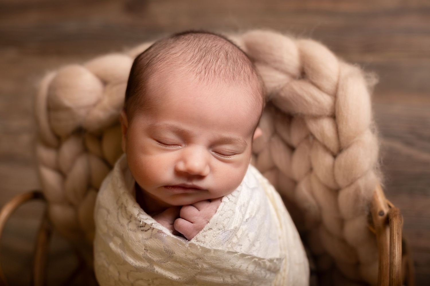 Peaceful newborn wrapped in white swaddle on wooden surface.