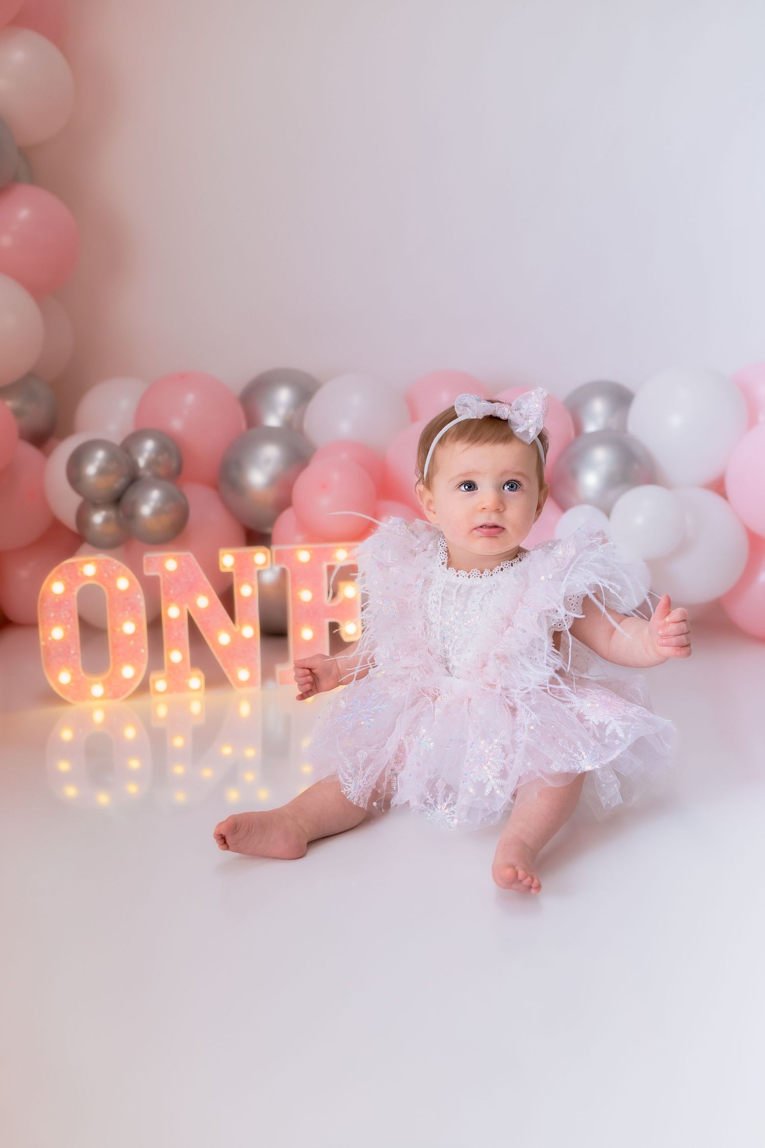 Pink and silver balloon display with illuminated 'ONE' sign for birthday photoshoot.