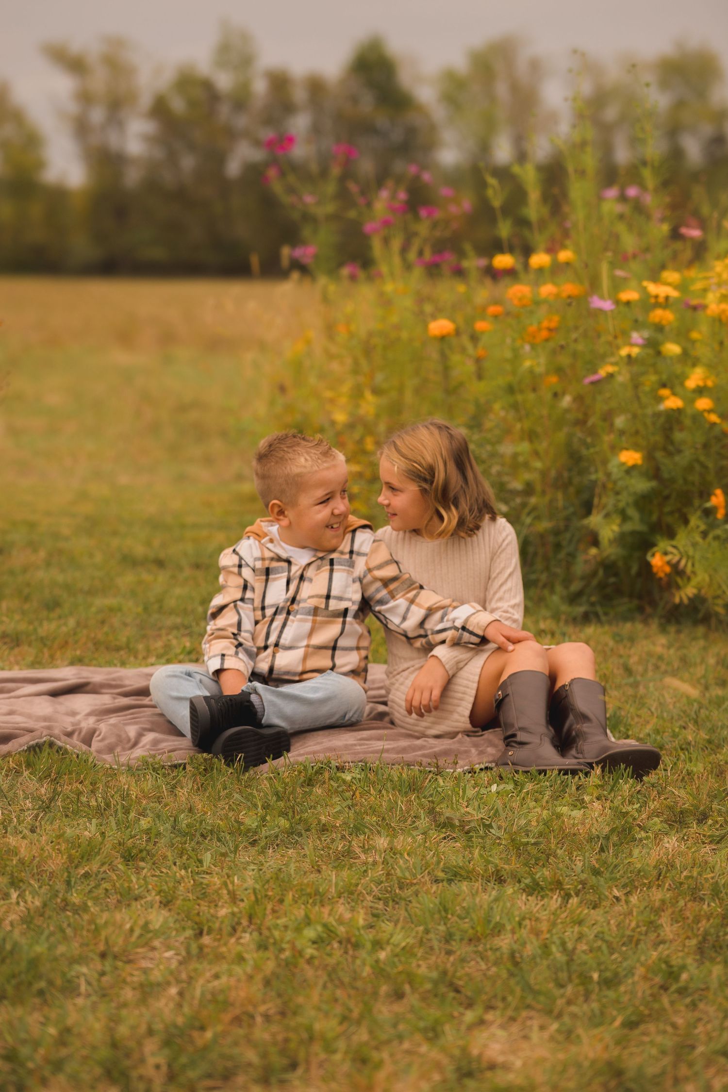 Two children sitting on blanket beside colorful wildflowers having candid moment together.