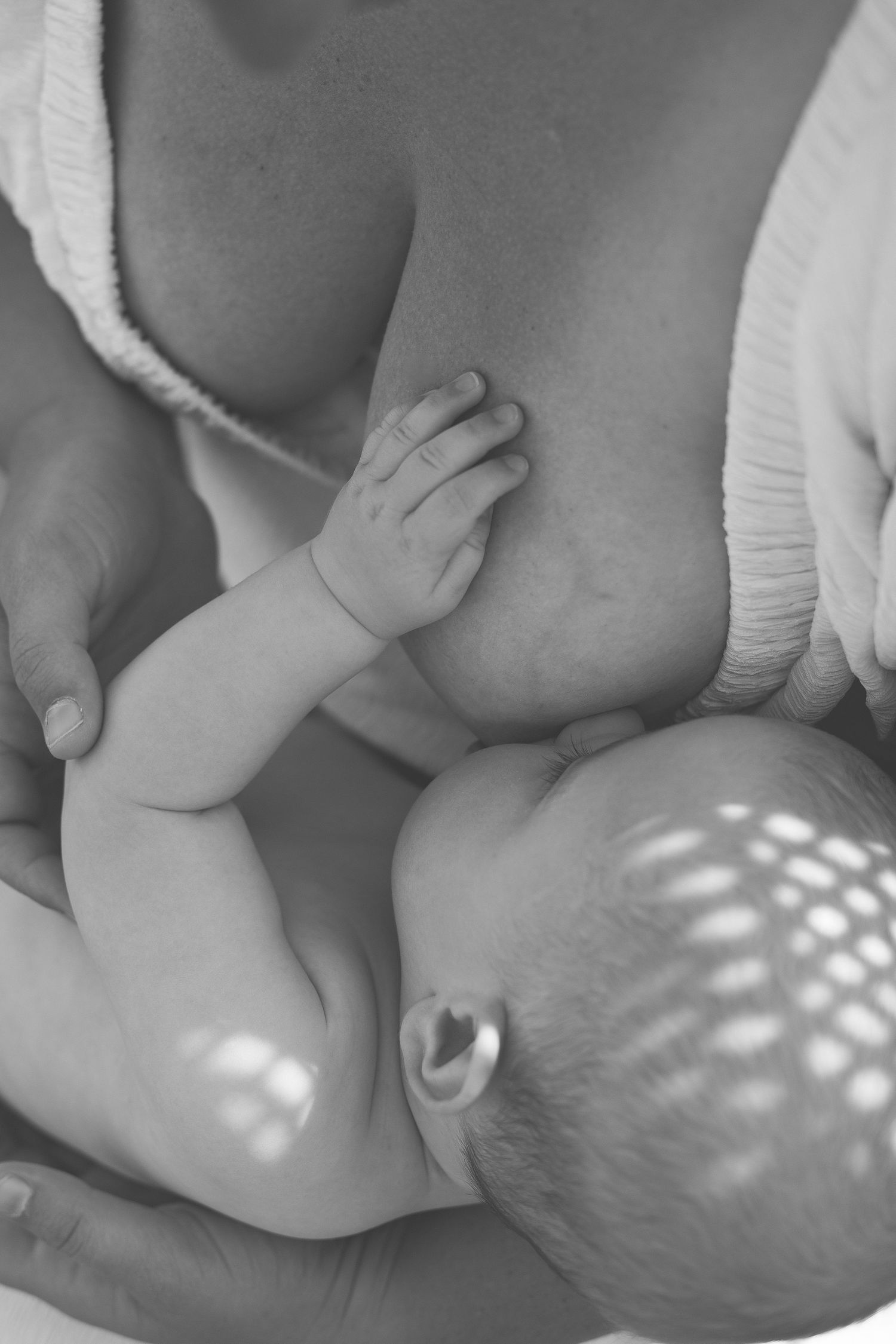 Intimate black and white close-up of a nursing baby's hand against soft natural lighting.