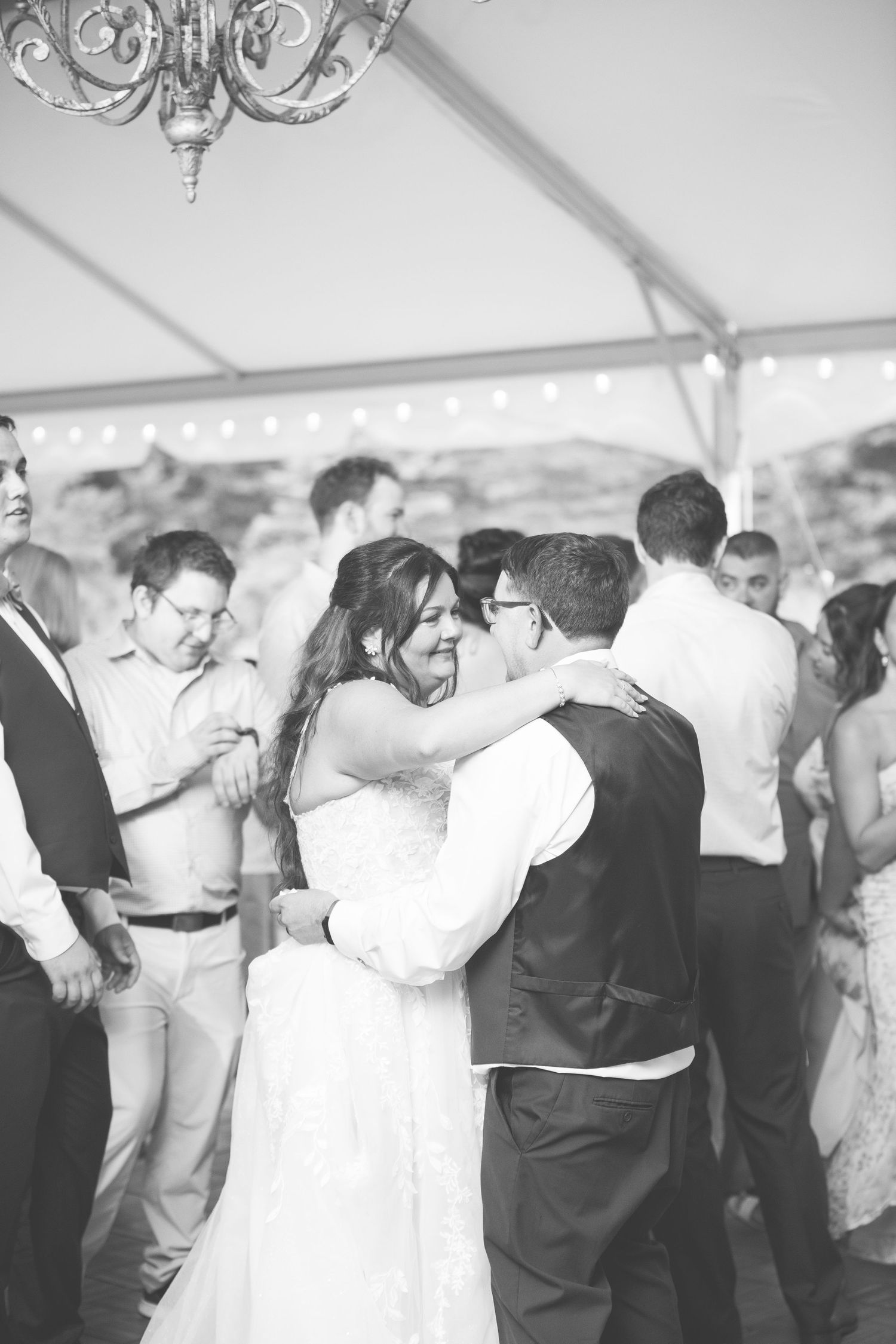 Wedding guests dance together under a white tent during a reception celebration.