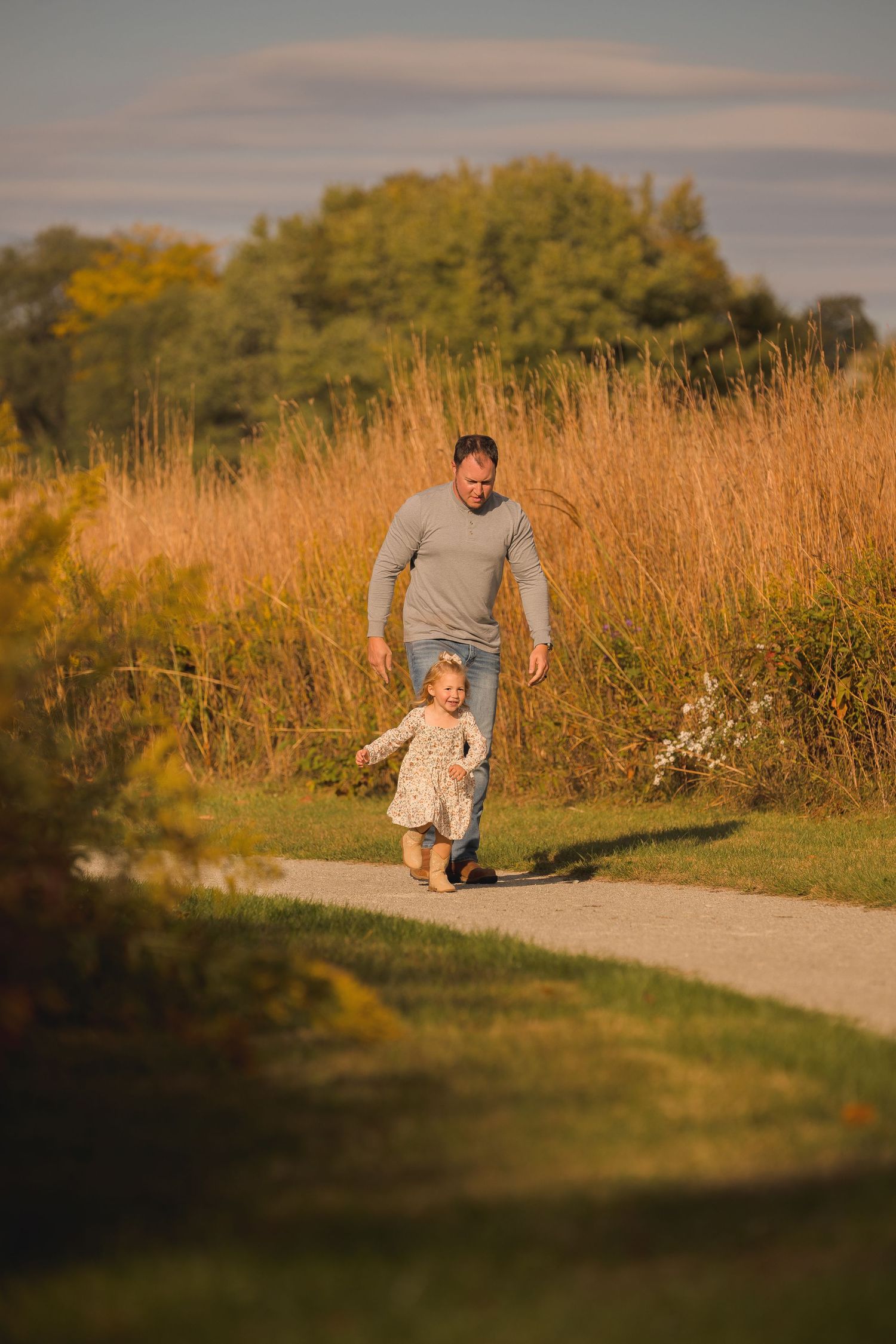 Parent and child walking together on a path through golden autumn grasses.