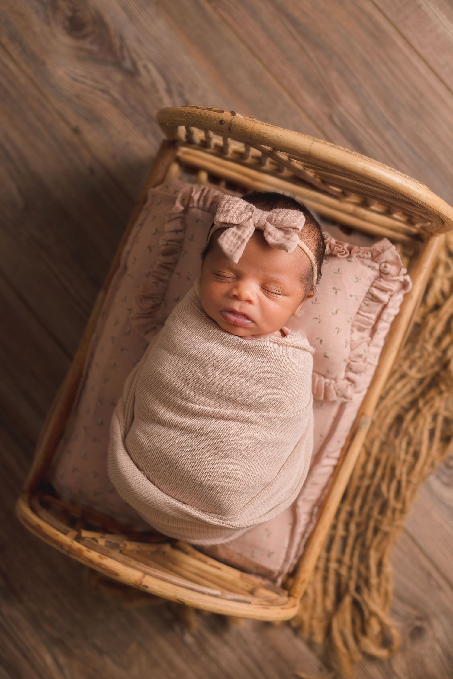 Artistic newborn portrait in wooden basket with pink swaddle and textured backdrop.