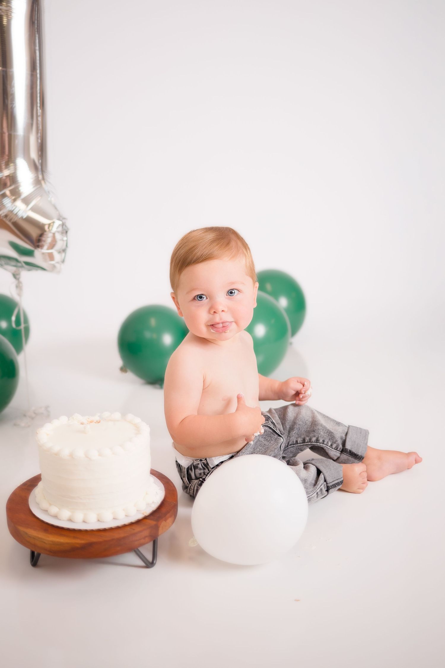 A first birthday photo shoot with a white cake and festive balloon decorations.