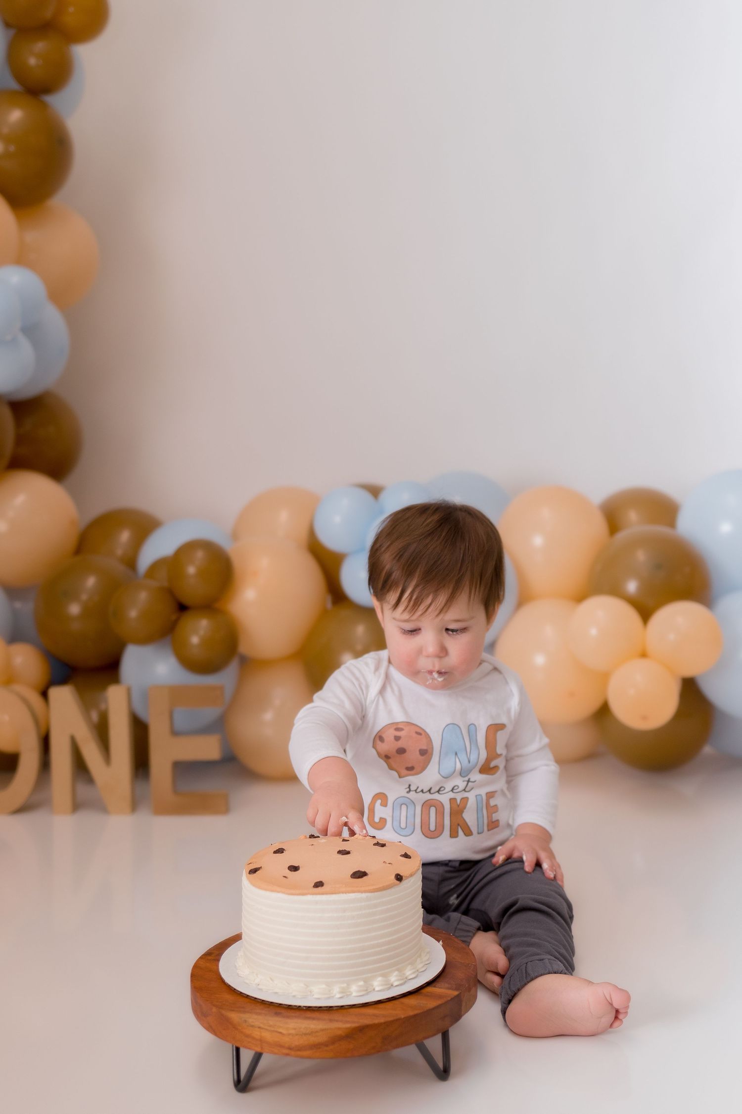 Birthday cake smash session with cookie-themed decorations and balloon backdrop.