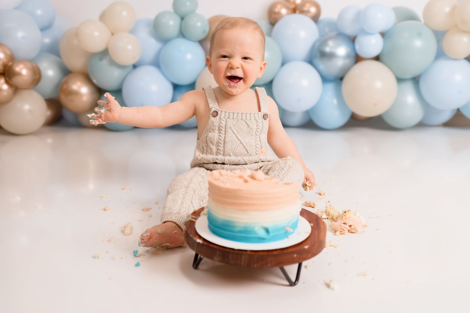 Baby enjoying cake smash photoshoot with blue balloon backdrop.