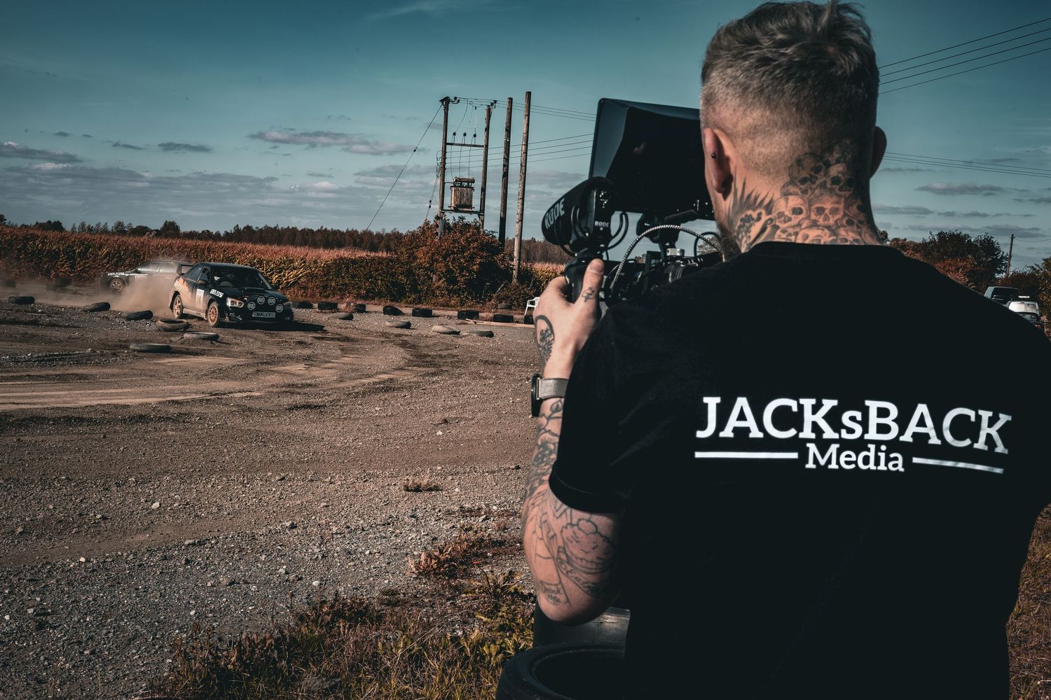 Tattooed videographer wearing JACKsBack Media shirt filming a car event outdoors. Hertfordshire, Cambridgeshire, UK