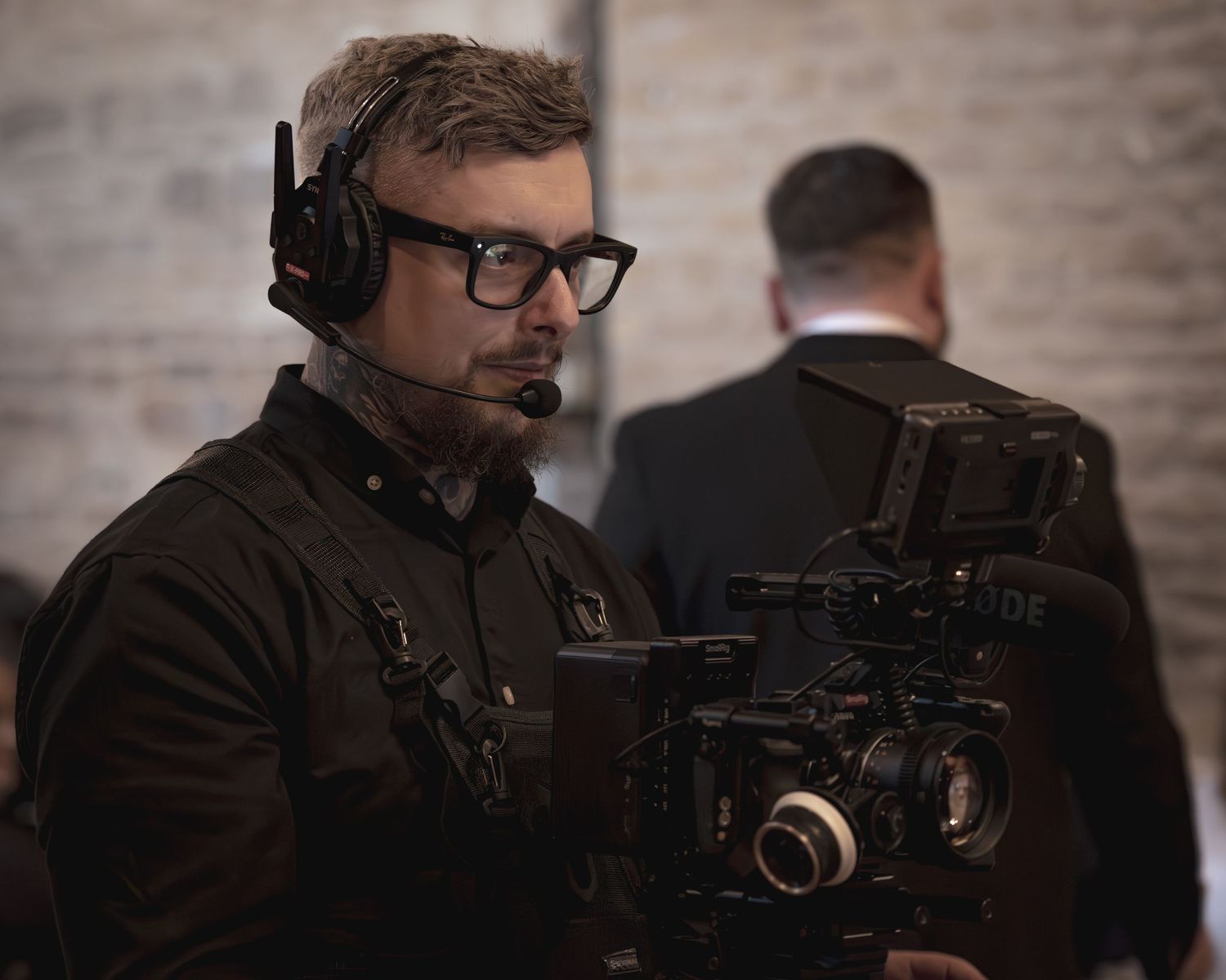 Focused videographer with headset and glasses operating a professional cinema camera indoors. Hertfordshire, Cambridgeshire, UK