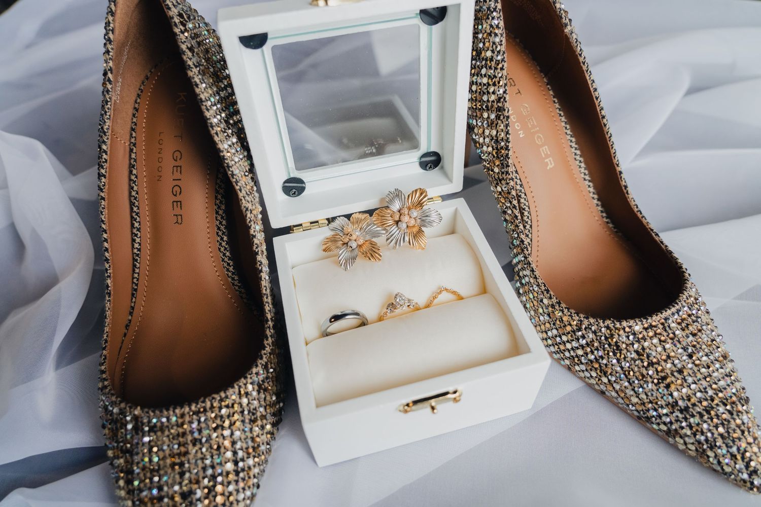 Elegant rhinestone-studded bridal shoes displayed on white fabric with jewelry box details.