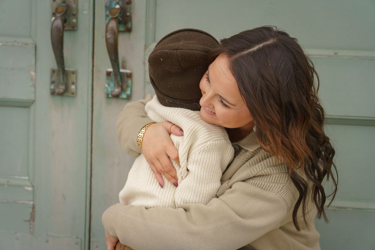 Two people sharing a warm embrace against a soft mint green wall.