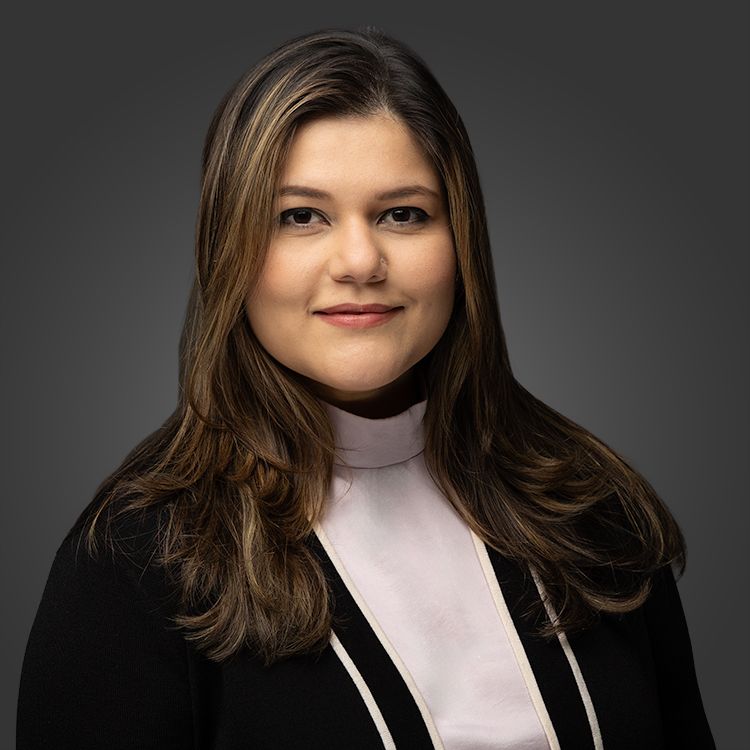Professional portrait of woman in black blazer and white top against dark studio background.
