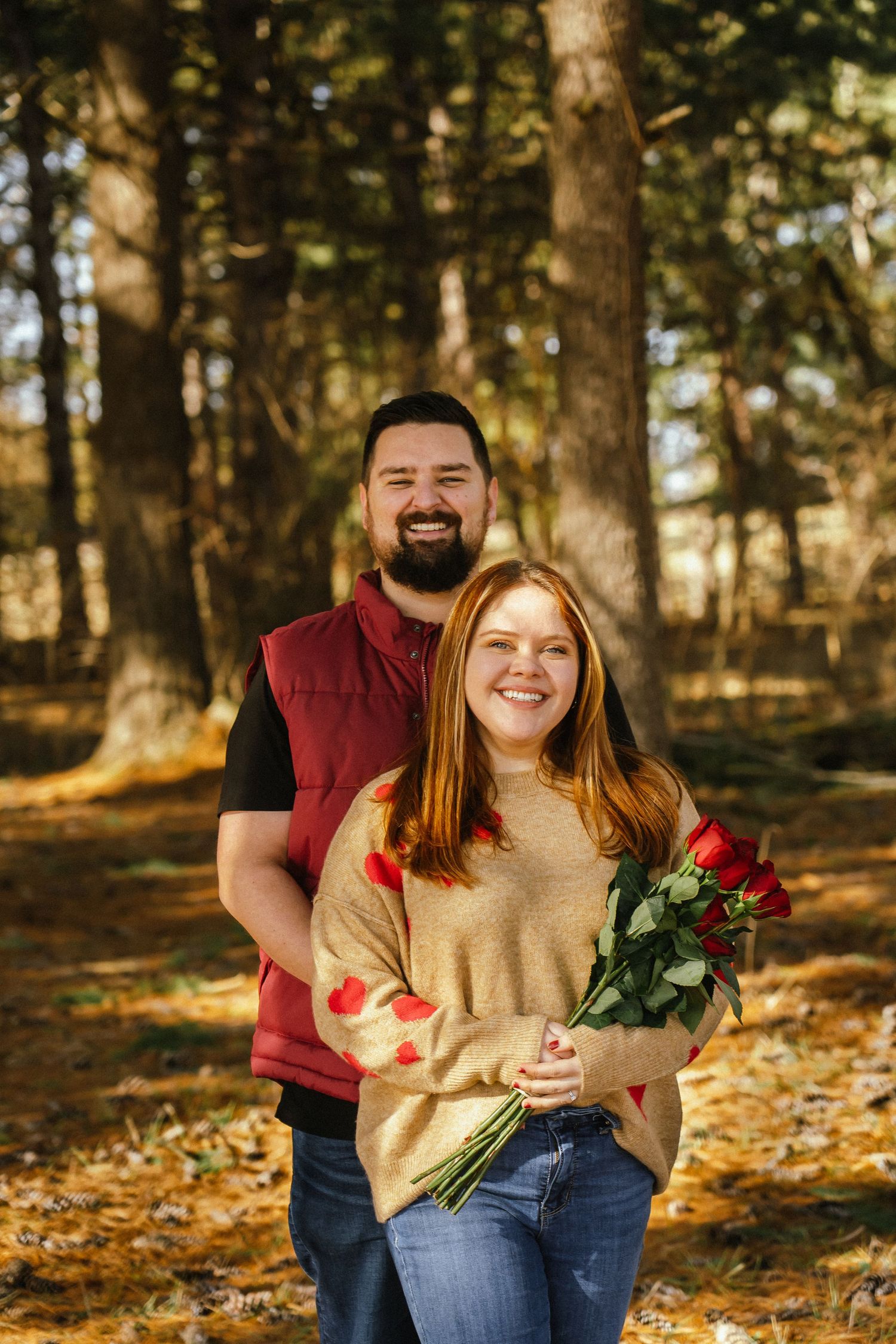 A couple enjoys a playful autumn photoshoot in a sunlit forest with fallen leaves.