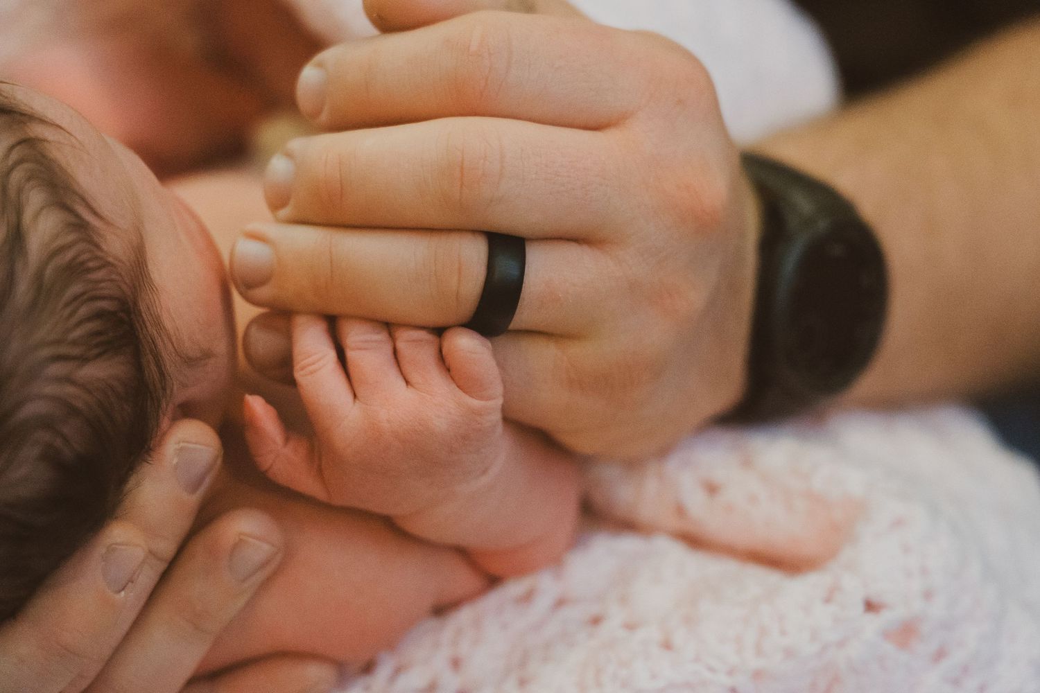 Close-up shot of hands holding a small baby's hand showing tender parental care and connection.