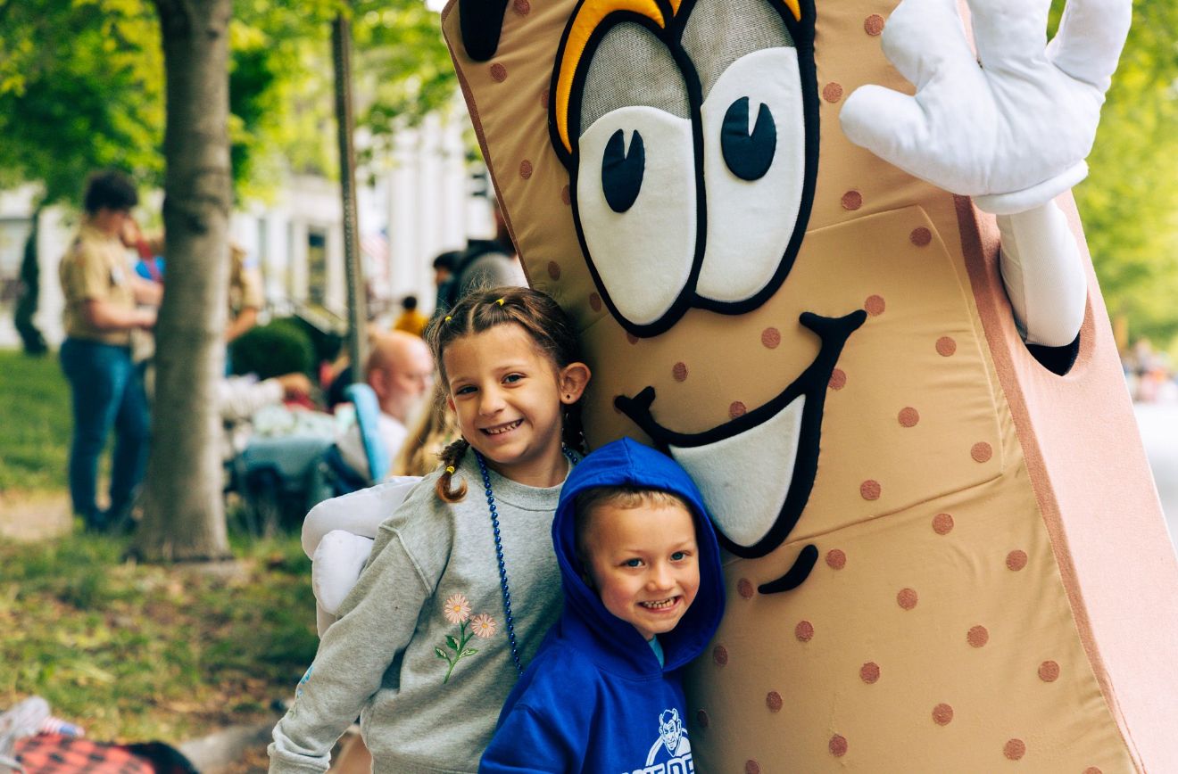 Cartoon mascot character with polka dots interacting with visitors at an outdoor event.