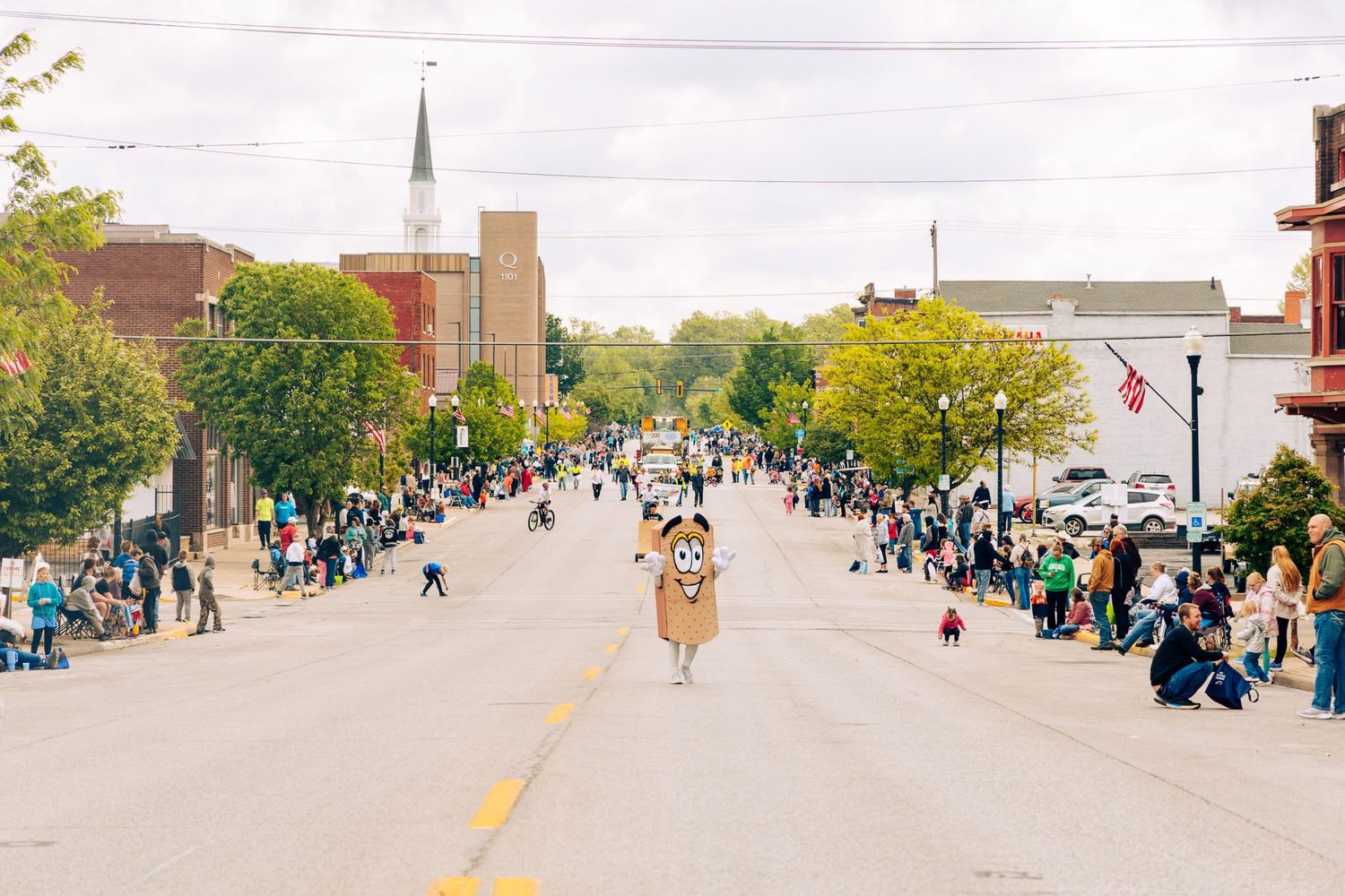 Aerial view of parade route with crowds lining both sides of small town street.