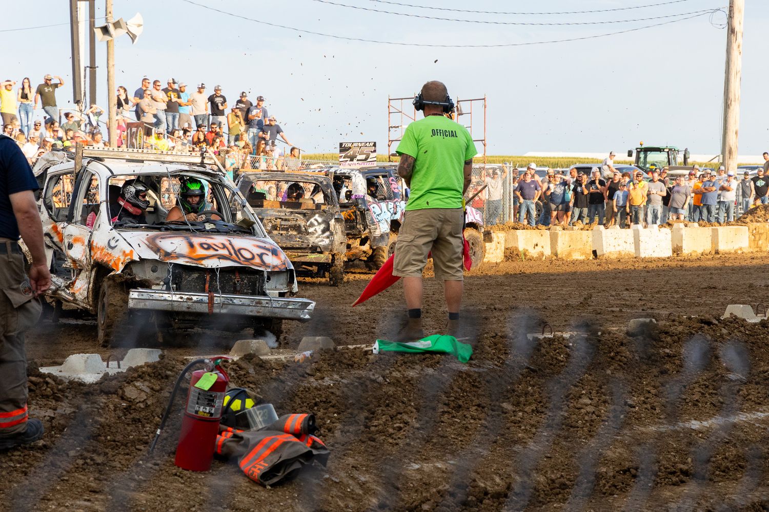 Demolition derby cars crash and compete in a muddy arena surrounded by spectators.