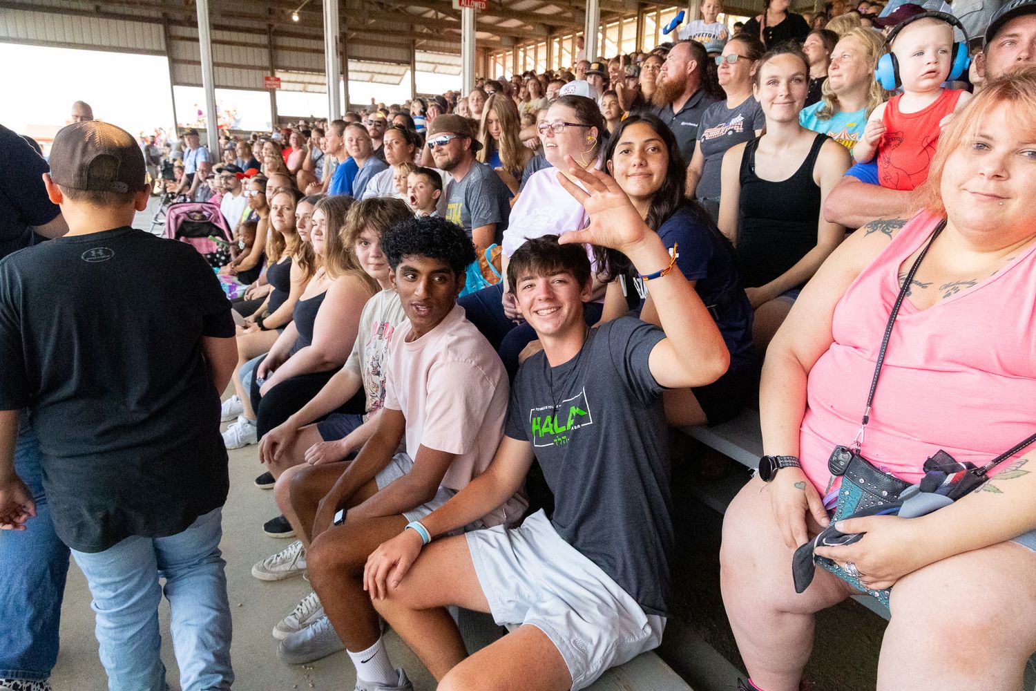 Large crowd seated in covered outdoor venue during daytime event.