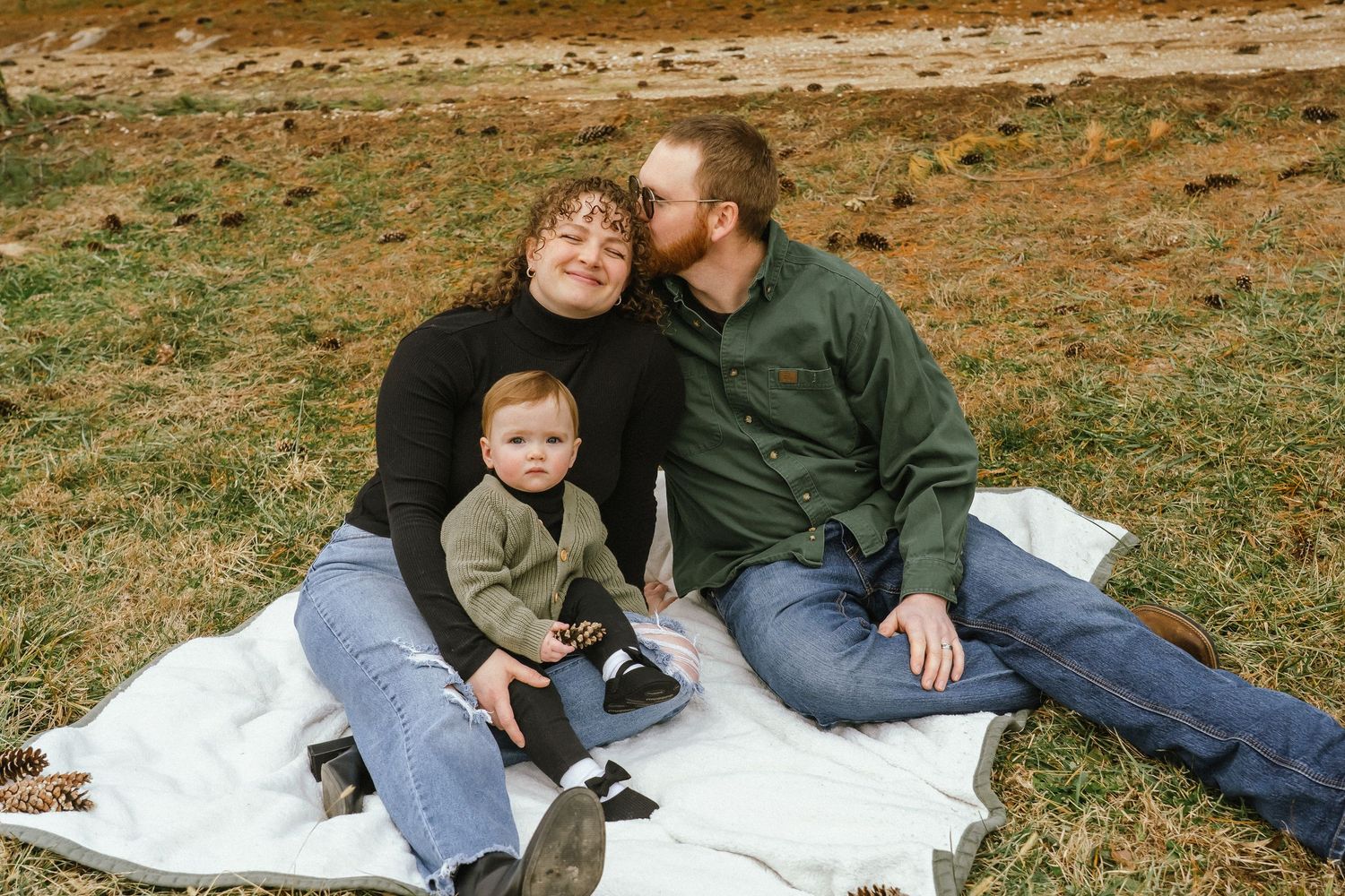 A family relaxing together on a white blanket in a grassy field during an outdoor photo session.
