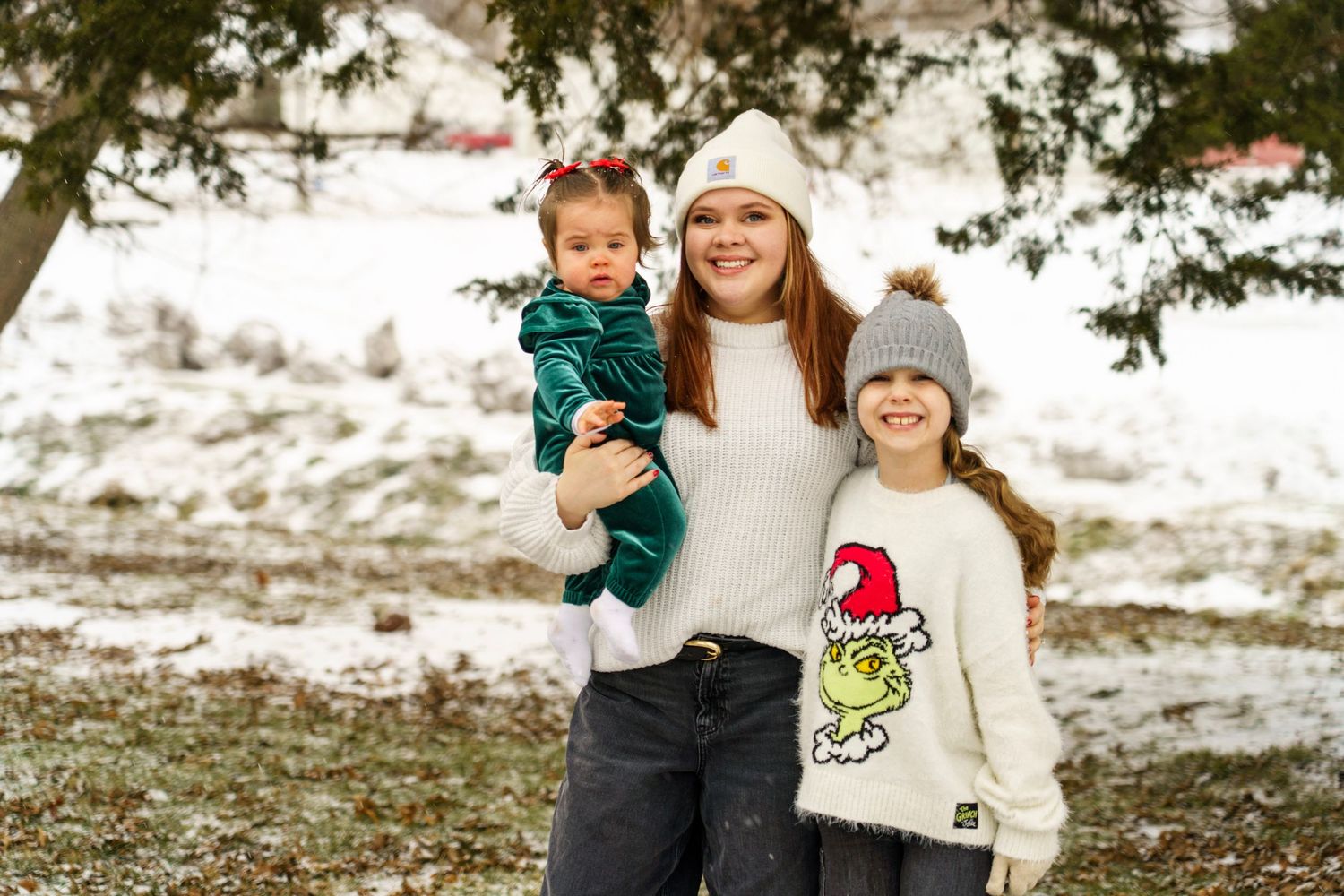 A heartwarming winter family portrait featuring matching holiday sweaters and knit hats in the snow.