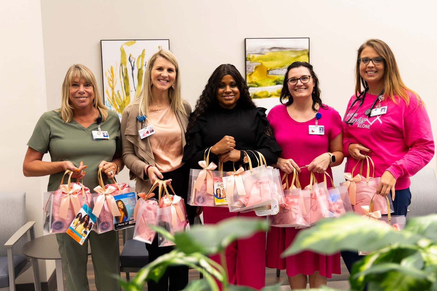 Team members displaying pink gift bags at office celebration event.